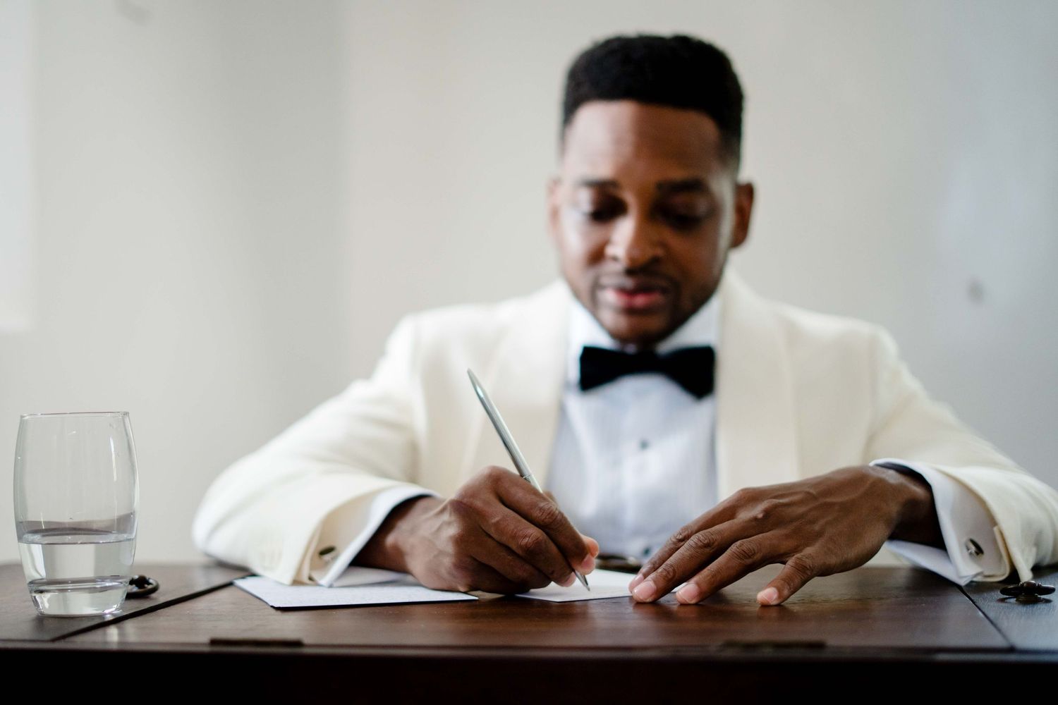 Medical professional in white coat writes notes while sitting at desk with glass of water.