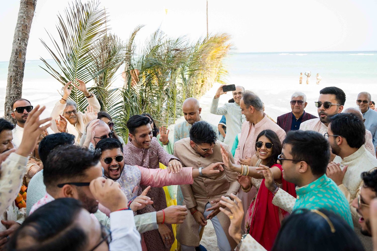 Enthusiastic crowd celebrates at an outdoor event with palm trees and ocean in the background.