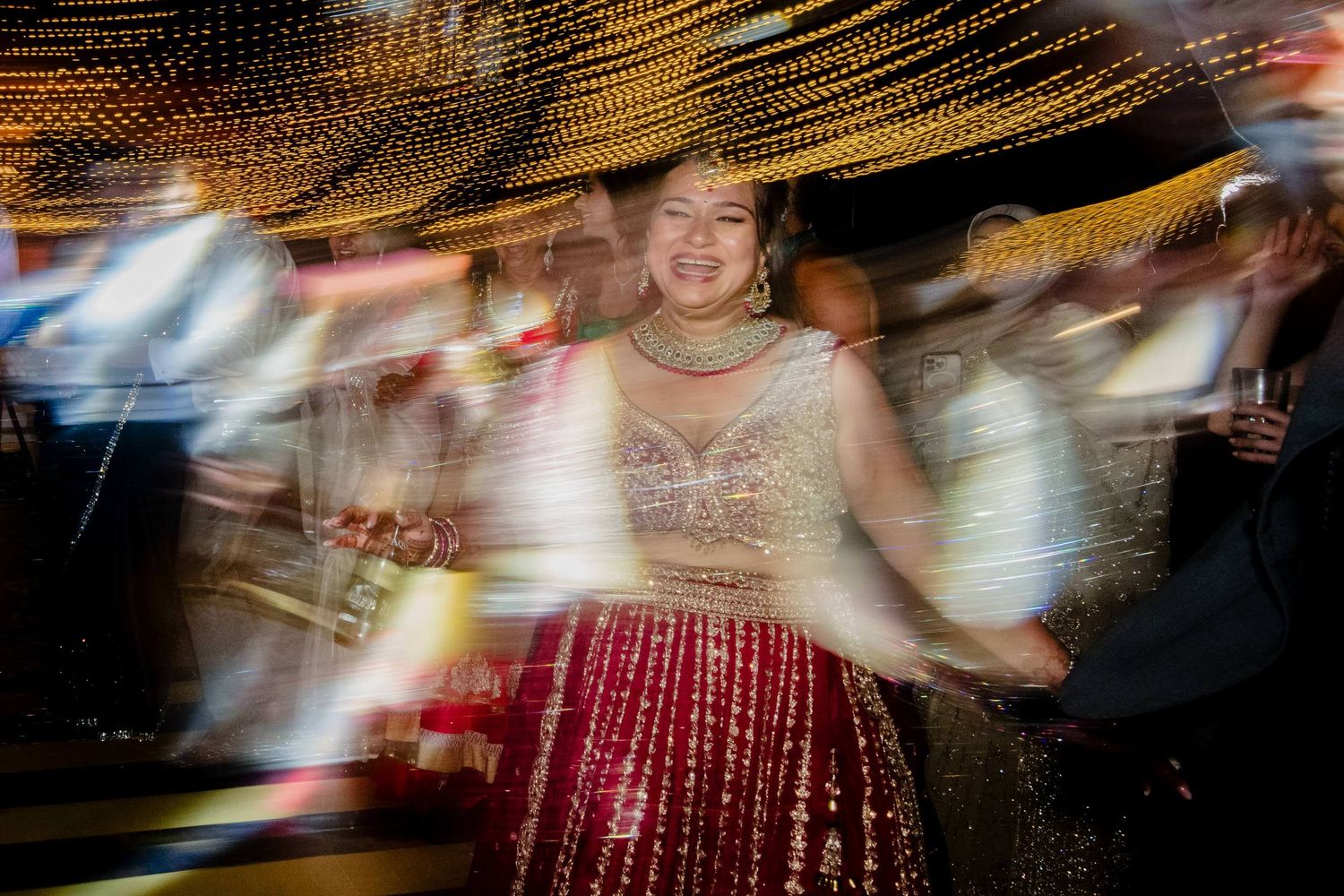 Motion blurred figure in red dress twirling under golden string lights creates a dreamy dance effect.