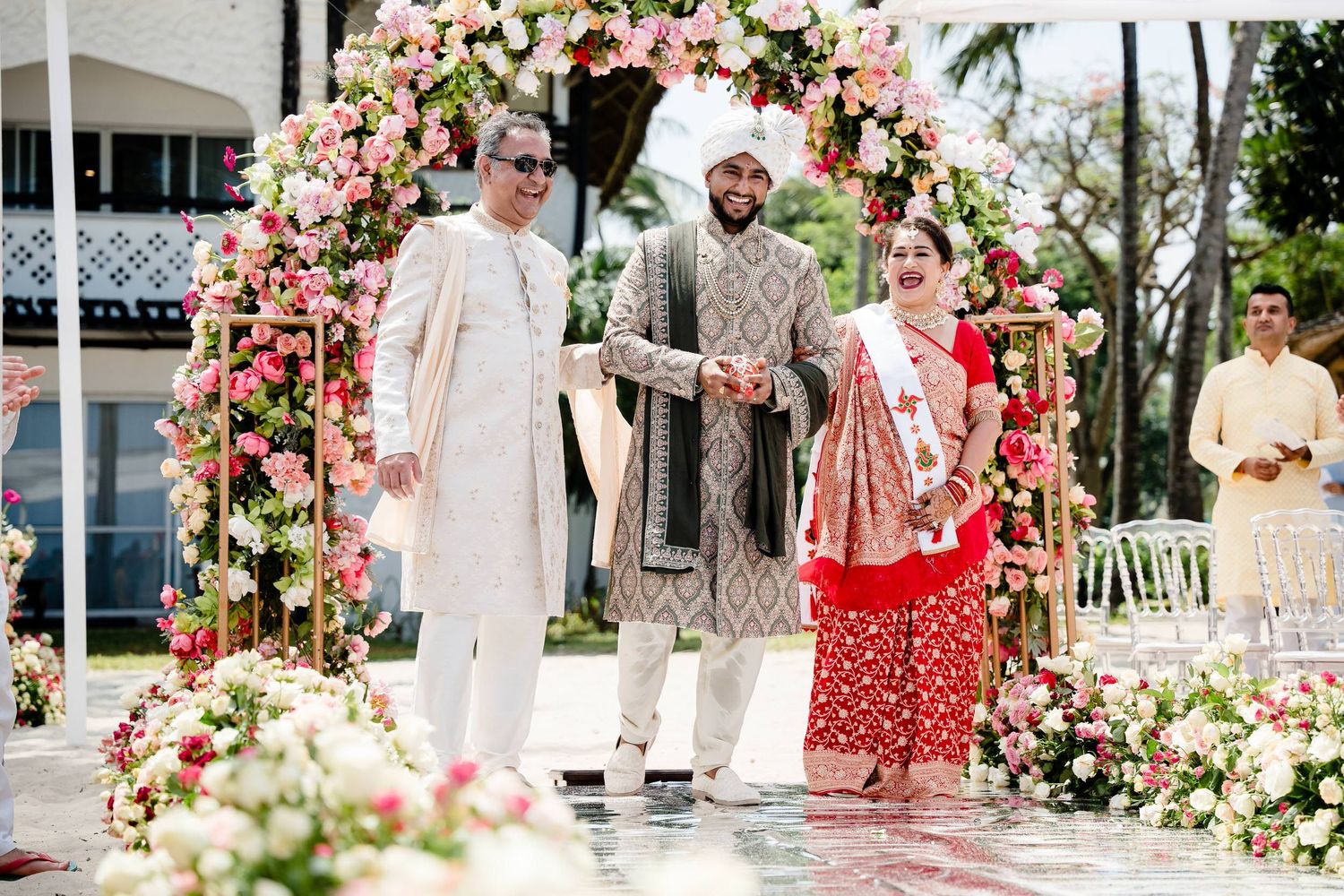 A wedding ceremony setup with pink and white floral arches and decorations in an outdoor garden setting.