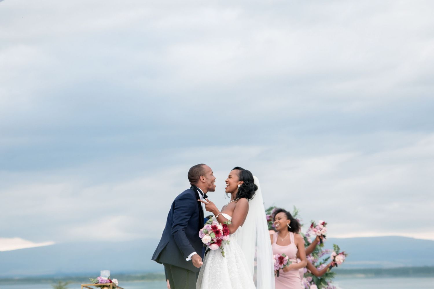 A romantic outdoor wedding ceremony with scenic mountains in the background and bridesmaids in pink dresses.
