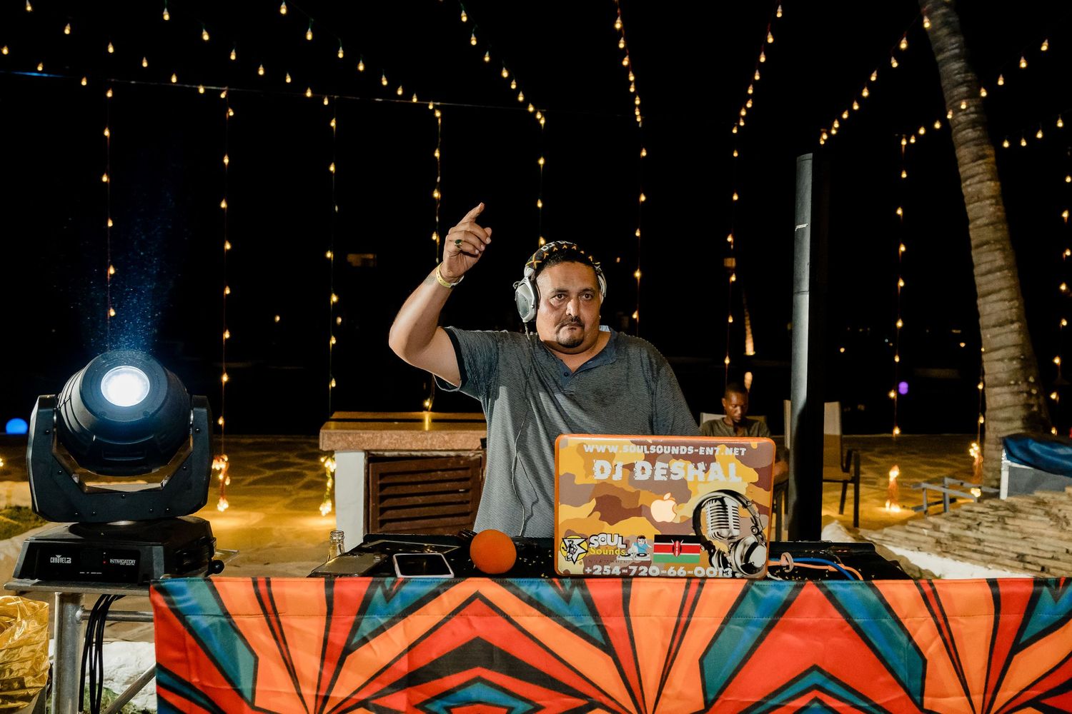 DJ performing at an outdoor event with decorative lighting and custom booth setup.