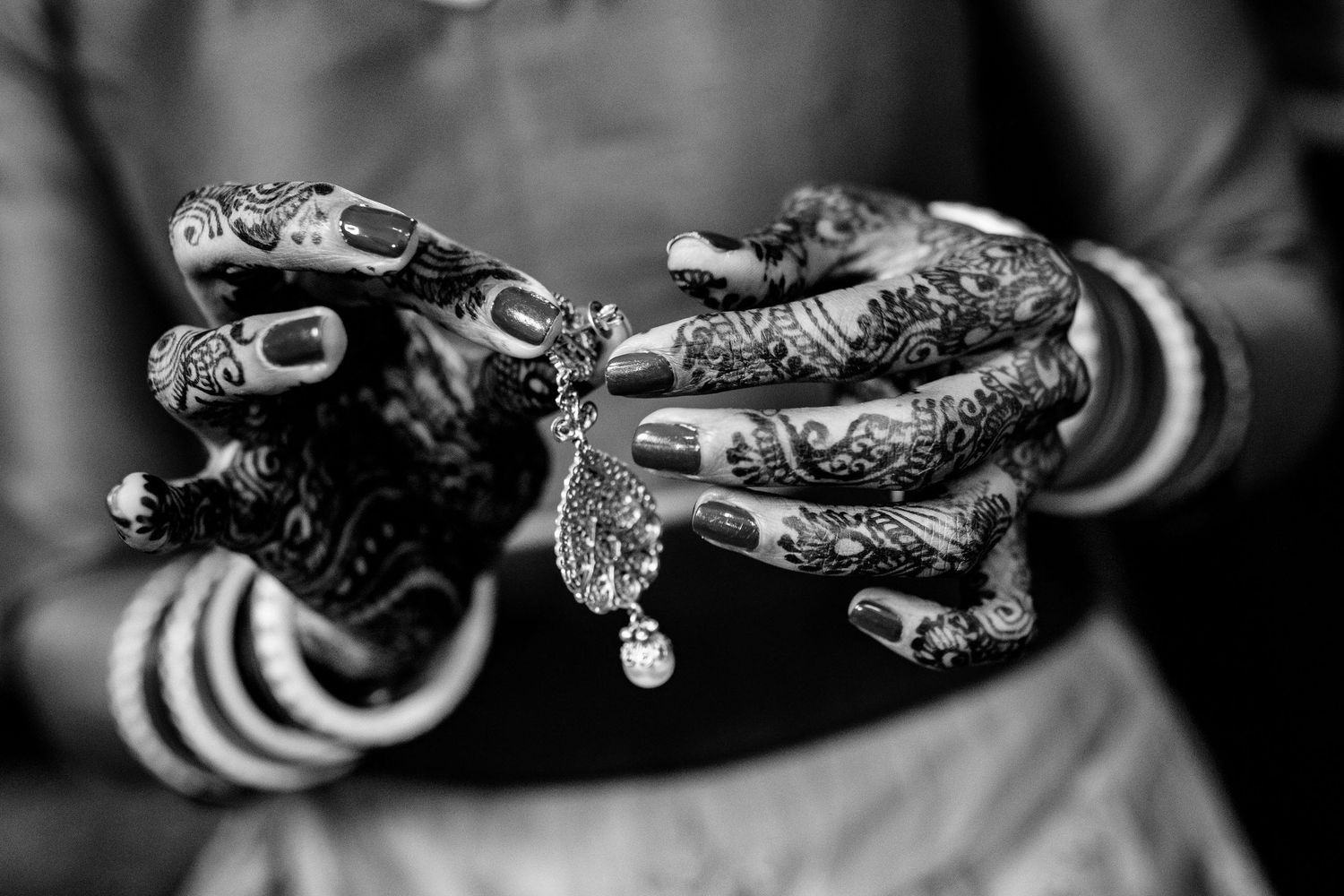 Close-up of hands adorned with henna and bangles holding traditional Indian wedding jewelry.