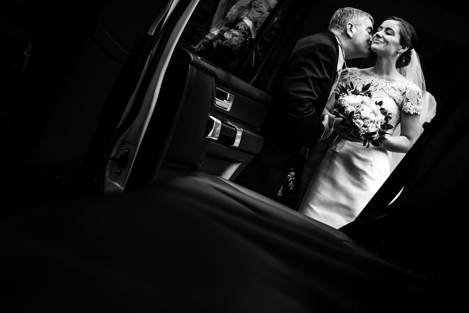 Tender moment captured in black and white as newlyweds embrace in classic car.