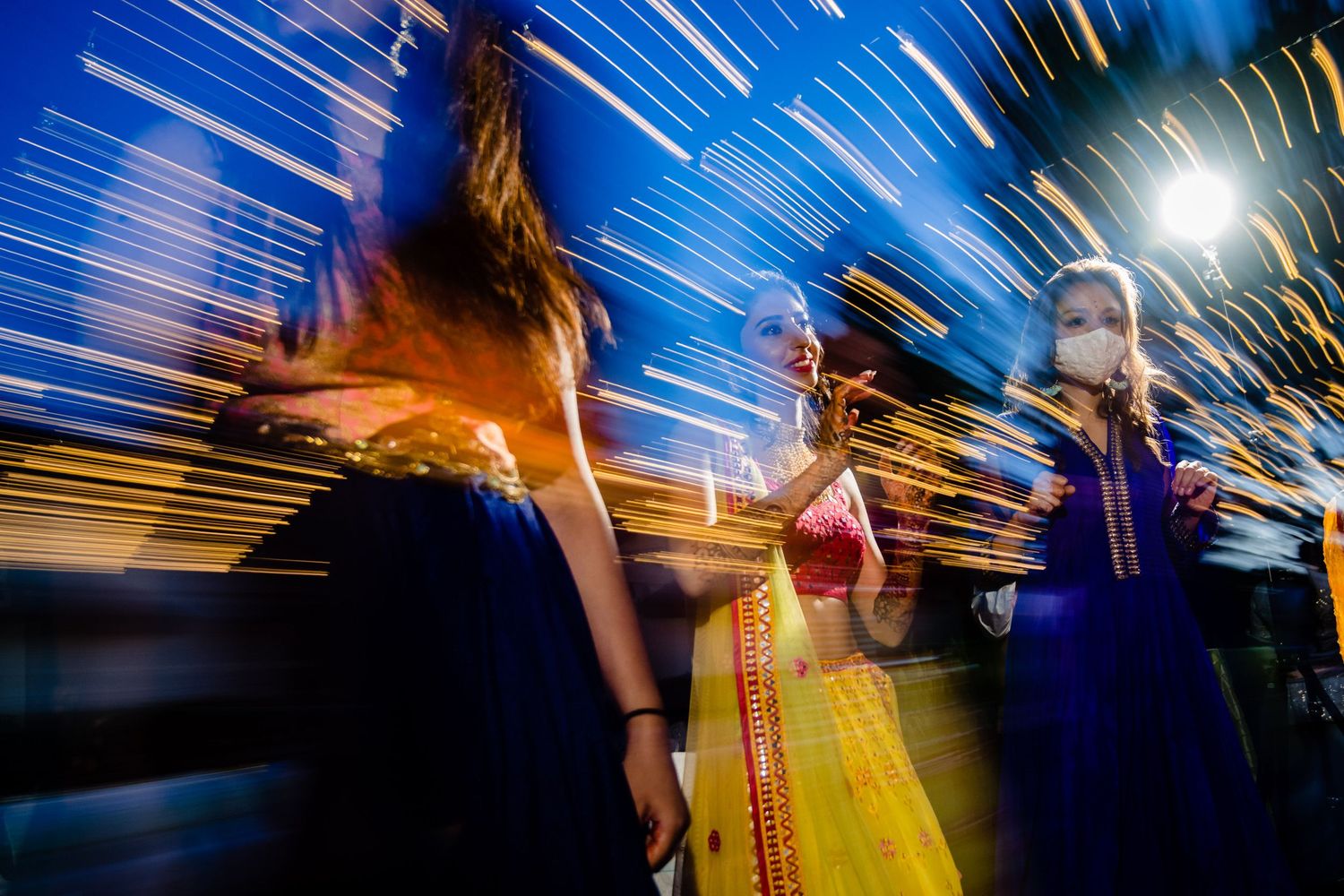 Long exposure dance photography creates streaks of light and motion on a blue background.