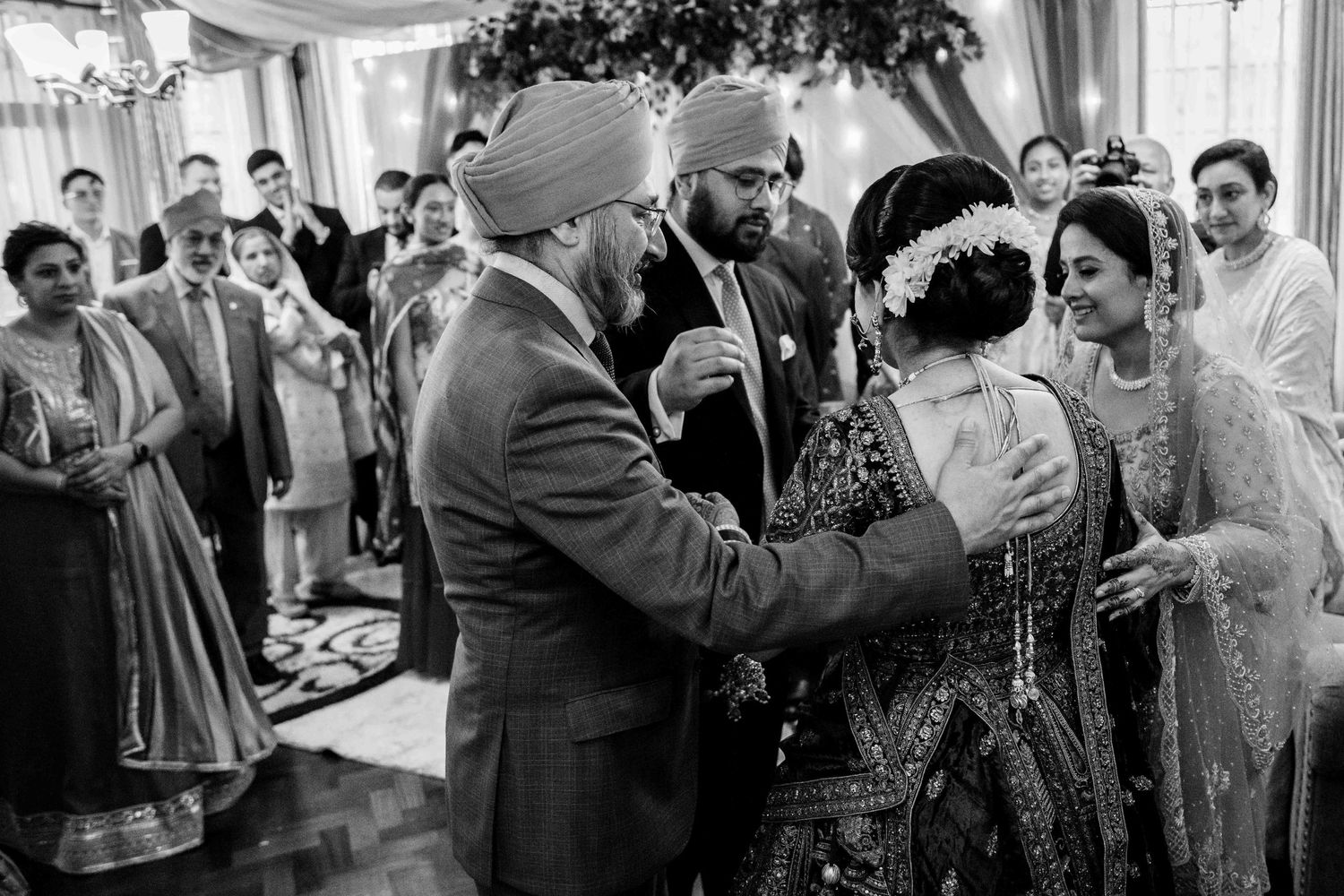 Black and white photo of a traditional Sikh wedding ceremony with guests gathered indoors.