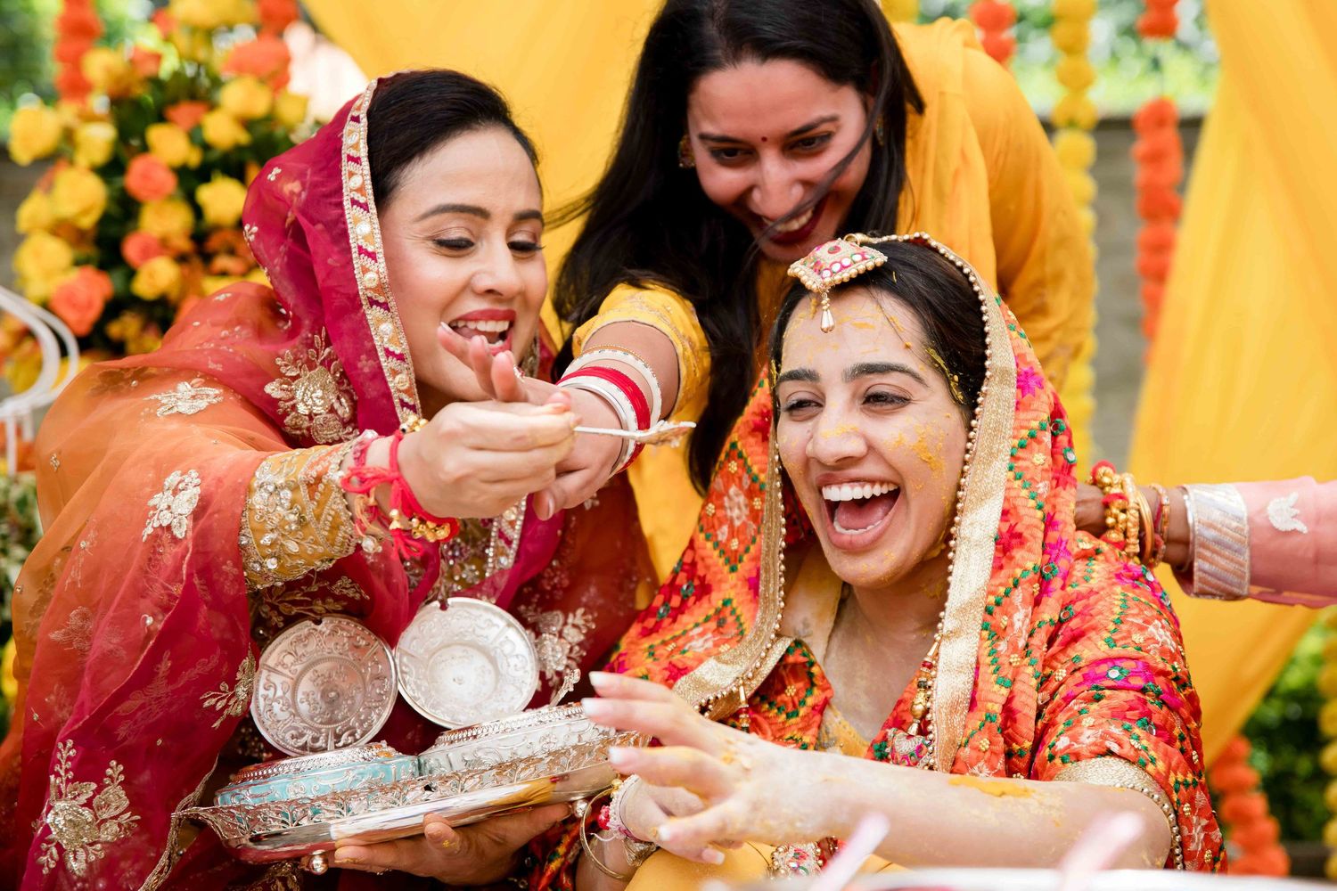 Women in traditional Indian attire sharing sweets and laughing during a celebration.