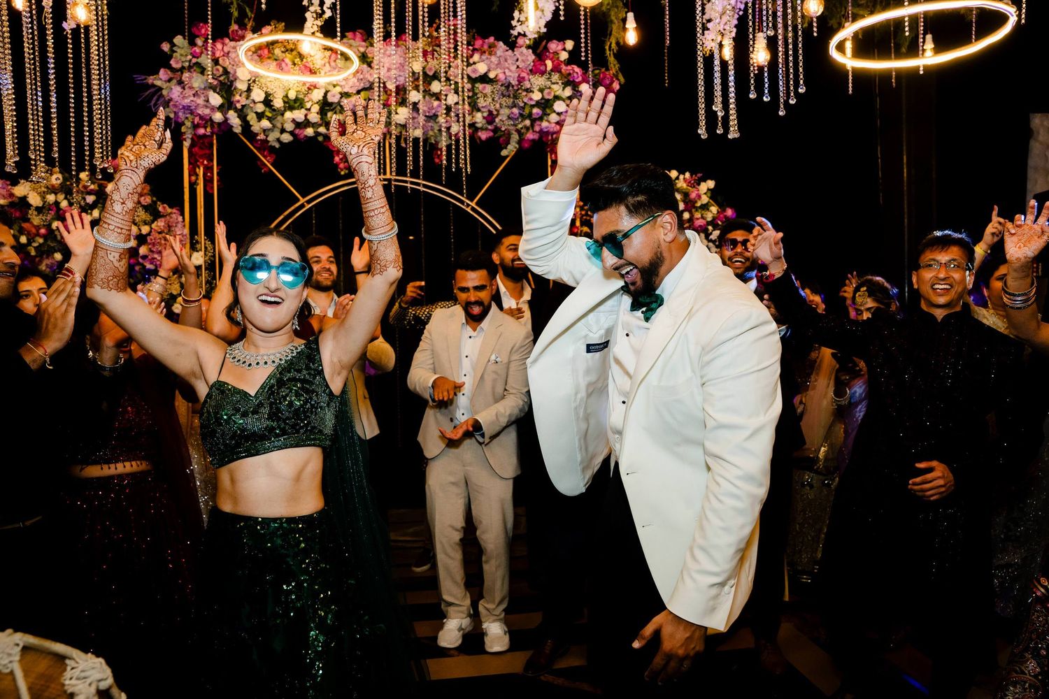 Wedding reception dance party with guests in formal attire dancing under hanging decorative lights.