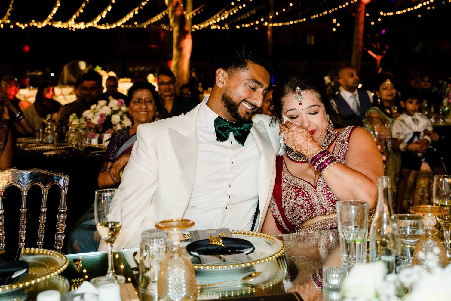 Wedding guests enjoy an elegant candlelit reception dinner at decorated tables with glowing string lights overhead.
