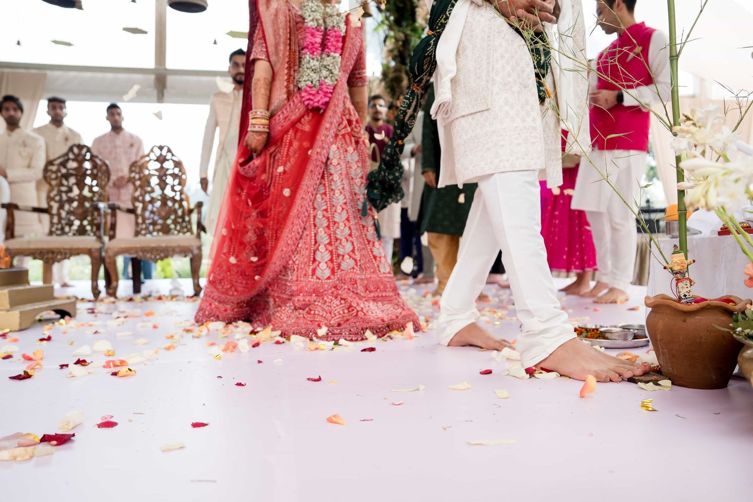Detail shot of wedding attire and rose petals scattered on white floor during ceremony.