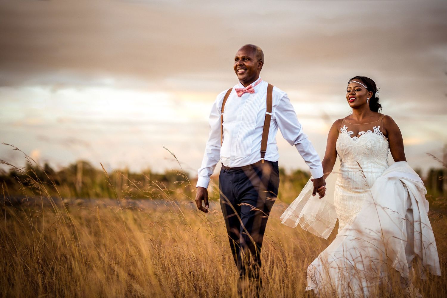Couple walking hand in hand through golden grass field at sunset.