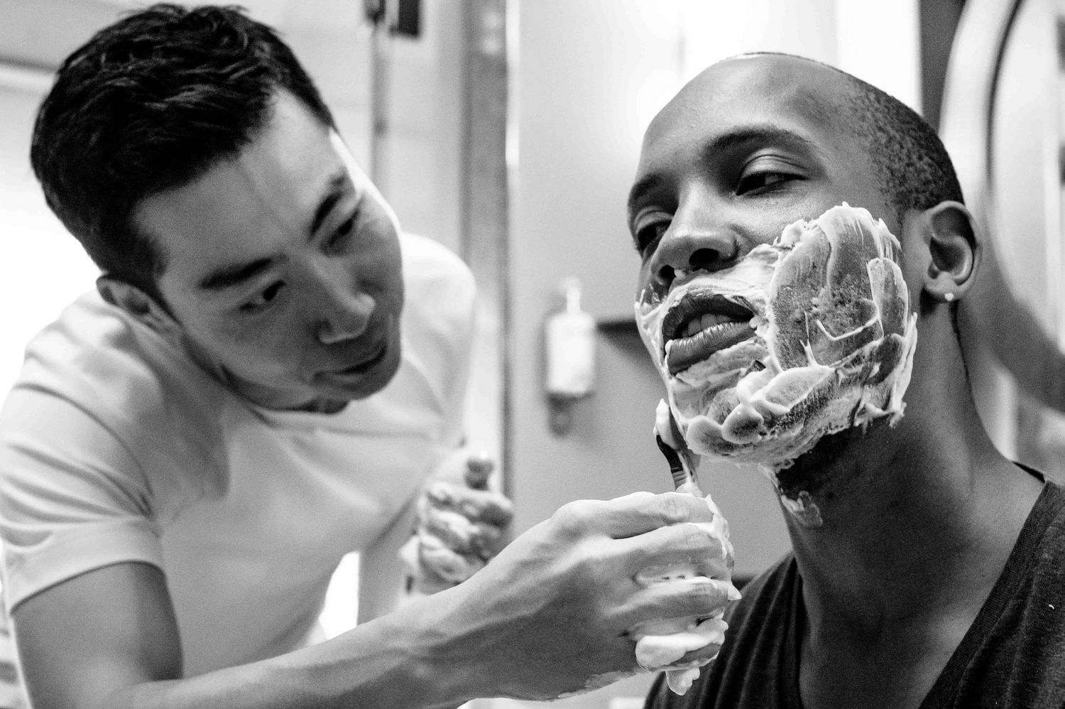 Black and white image showing a person getting a traditional straight razor shave at a barbershop.