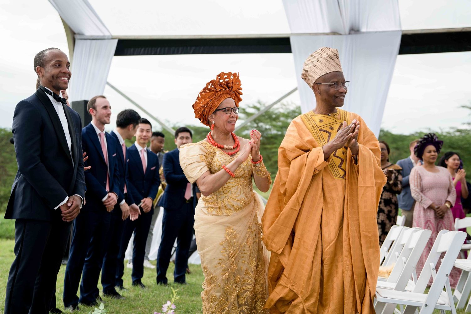 Wedding guests in traditional African attire celebrate during an outdoor ceremony.