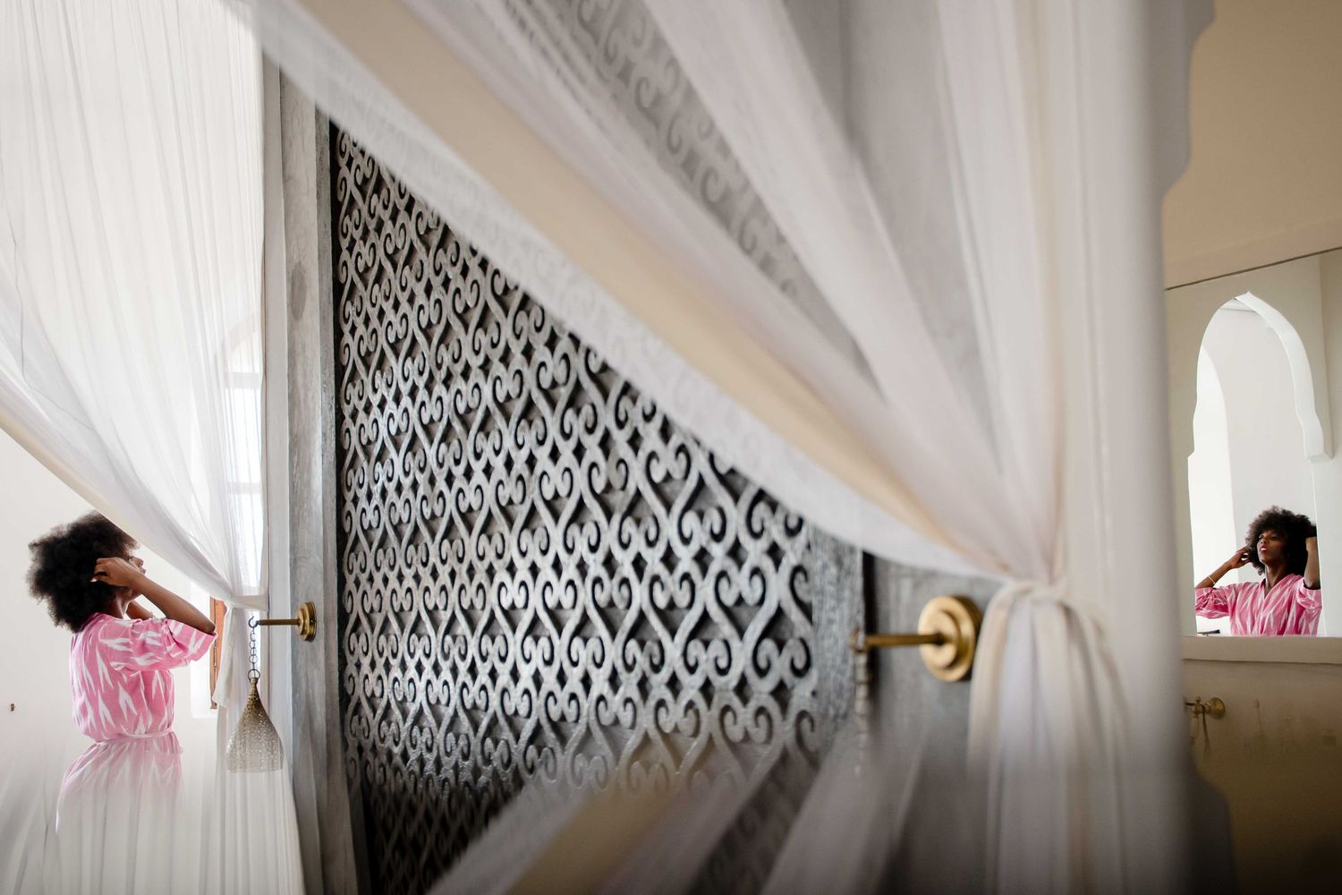A black and white damask wallpaper accent wall creates an elegant backdrop in a bright white room with decorative trim.