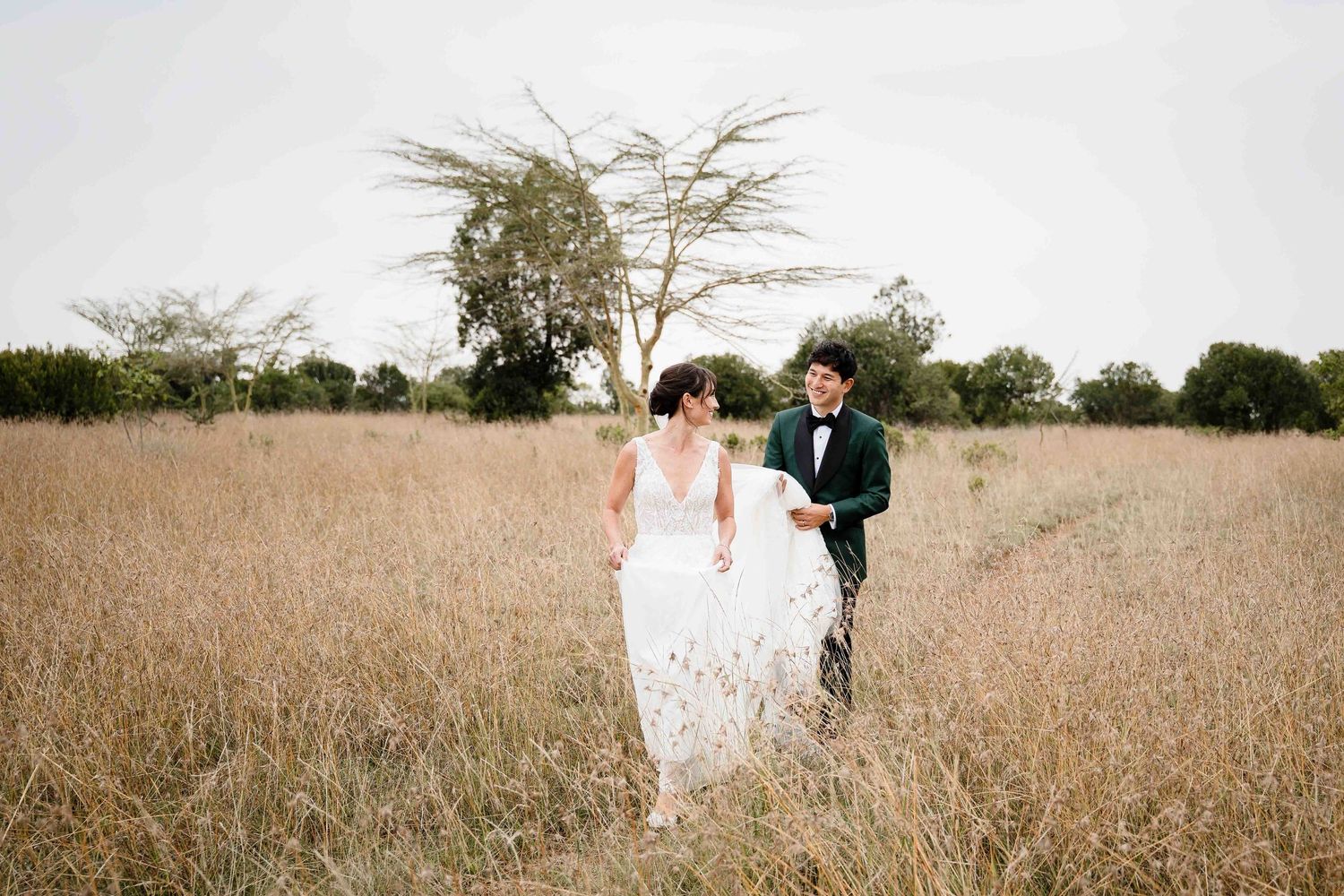A couple in wedding attire stands together in a golden wheat field during sunset.