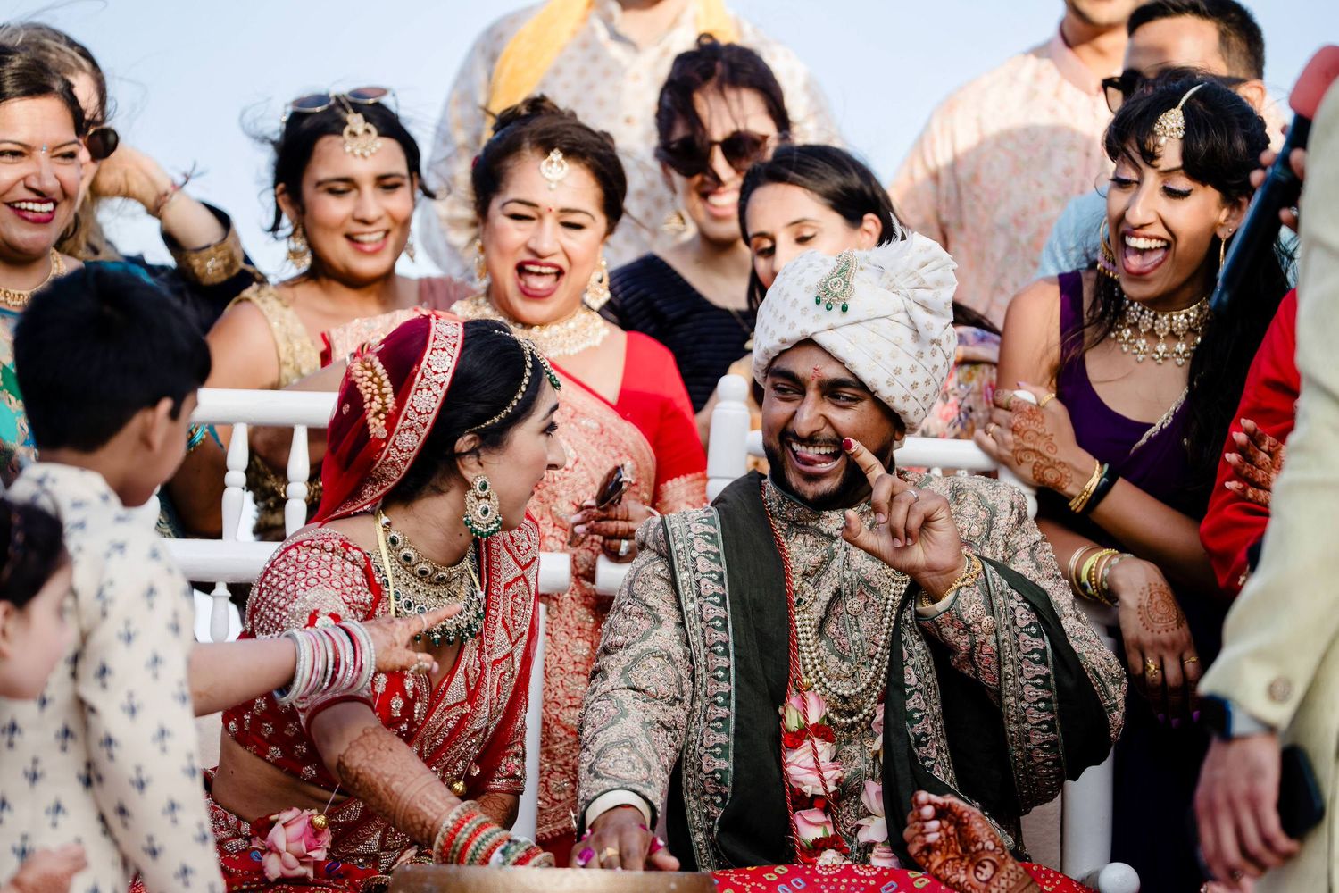 A joyful group of wedding guests celebrate and laugh together during a traditional Indian wedding celebration.