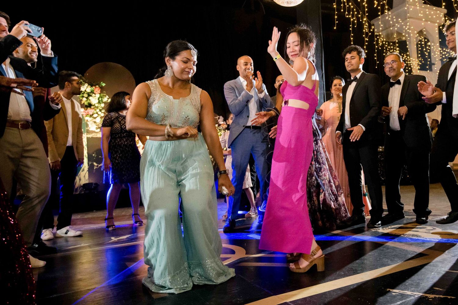 People dancing and celebrating at a nighttime party on a light-up floor with festive decorations.