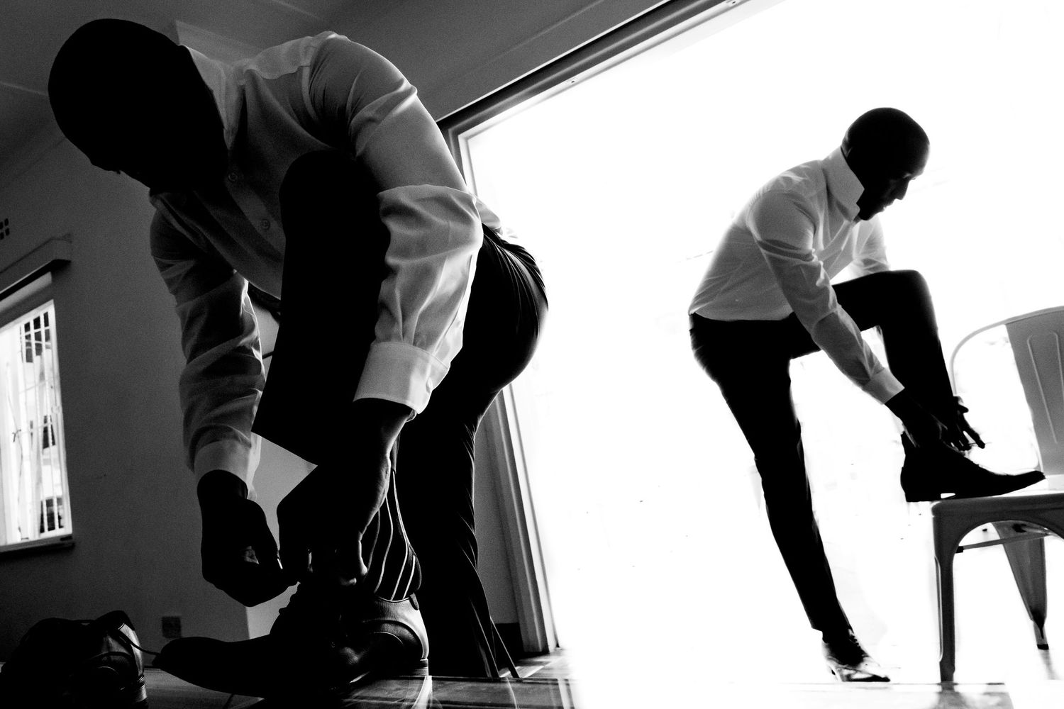 Two silhouettes in black and white showing people putting on shoes or boots.
