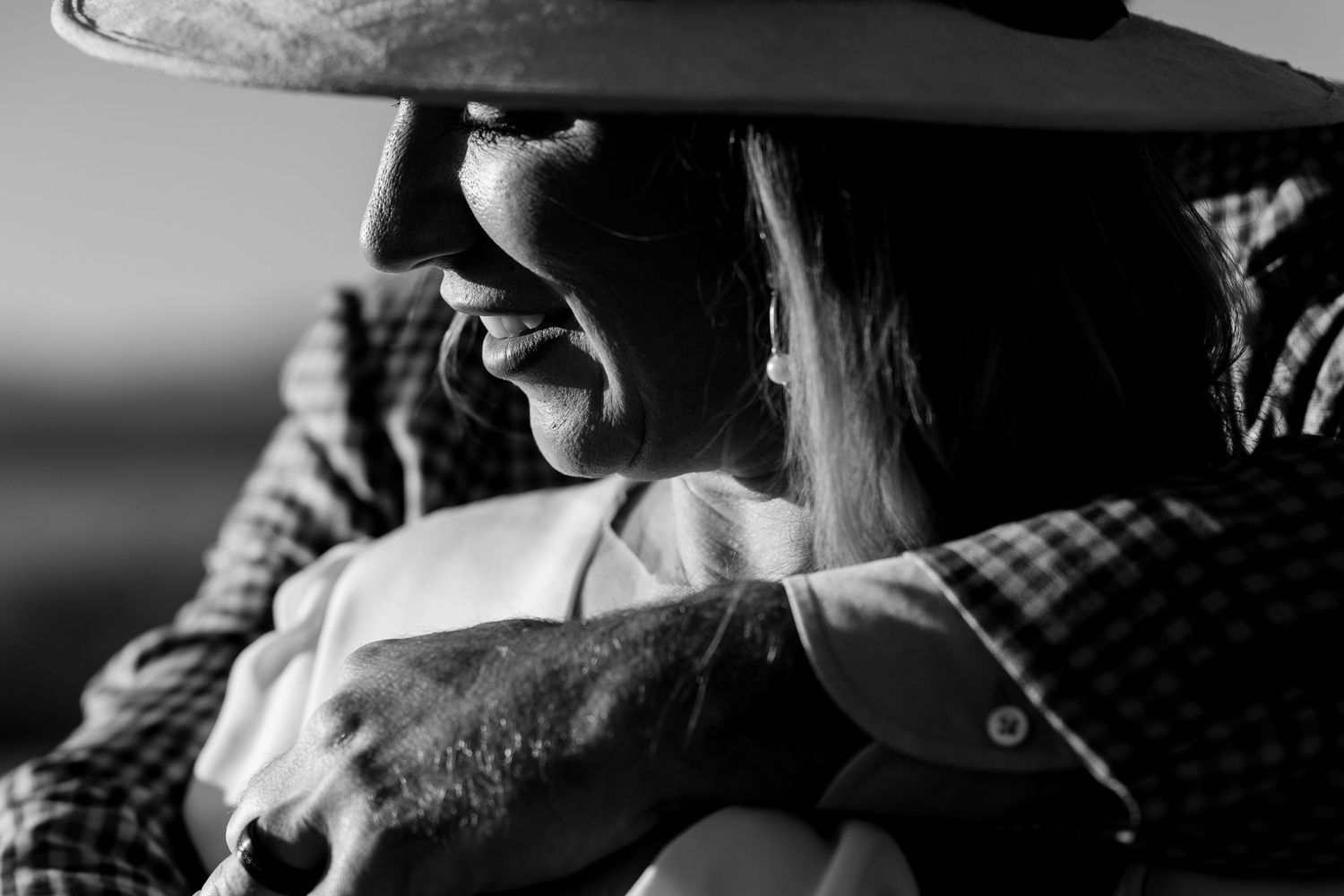Black and white close-up of a couple embracing with a western hat in focus.