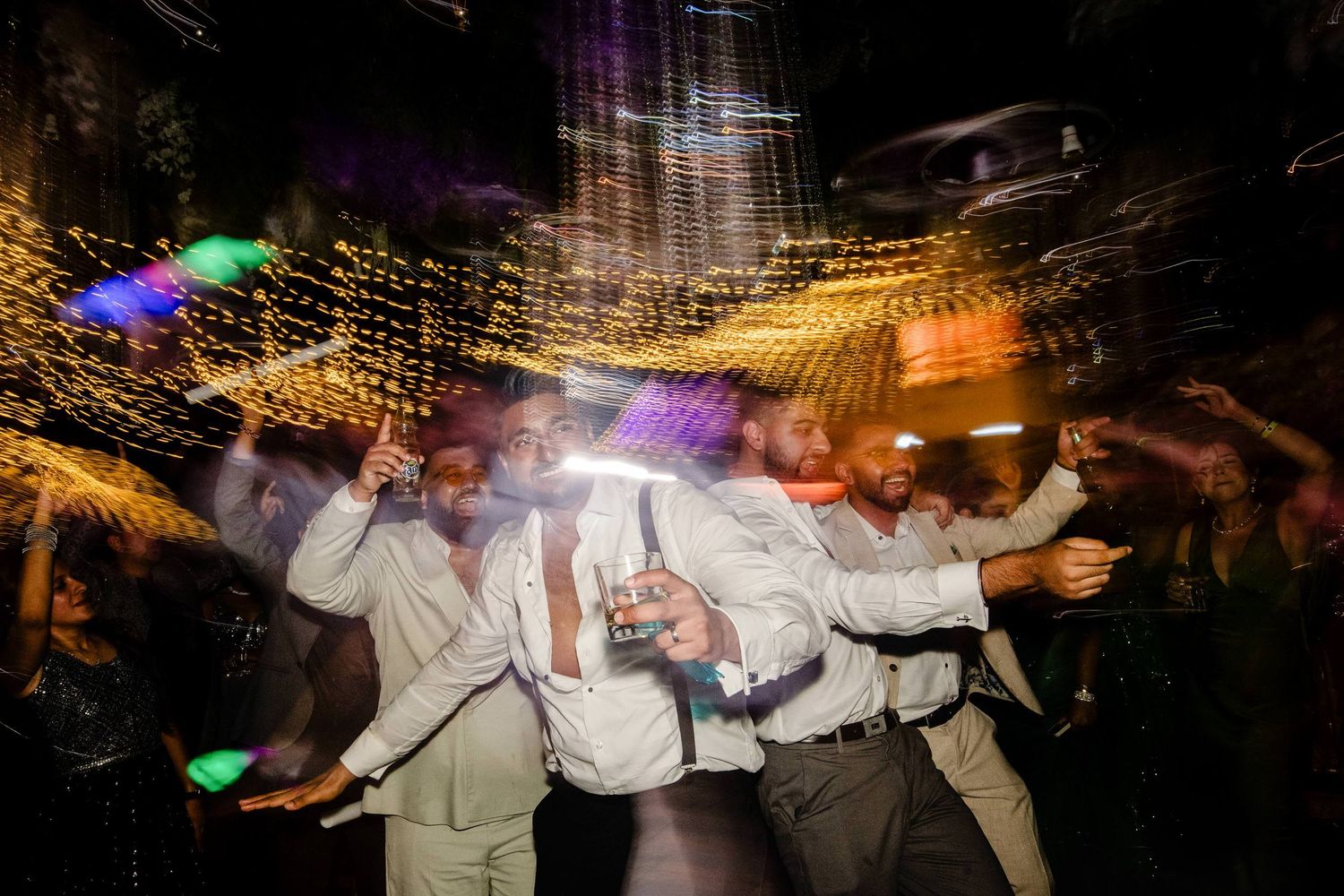 Wedding guests dancing under twinkling lights at a nighttime reception with dynamic movement.