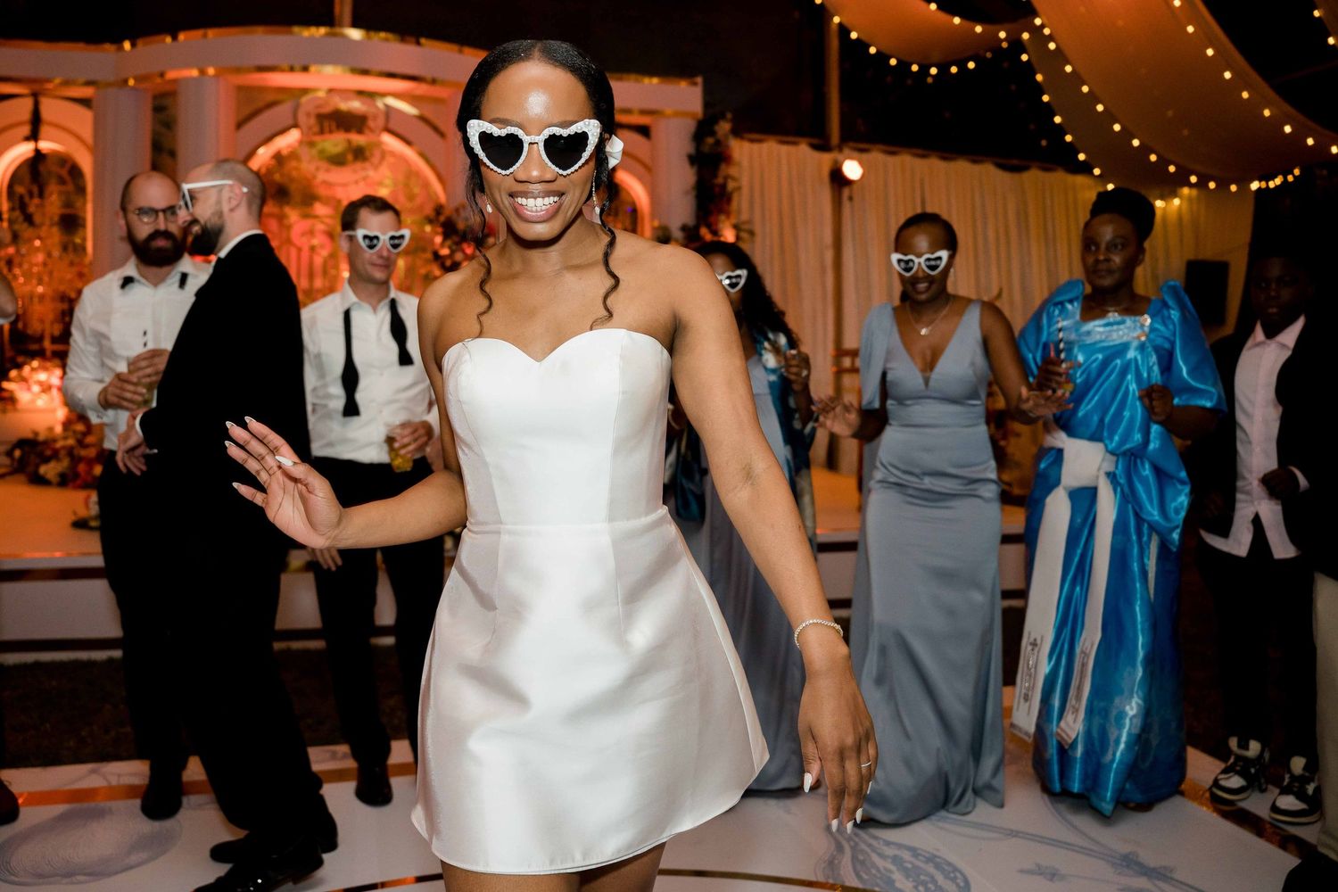 Wedding guests dancing together on the dance floor at an indoor reception with orange ambient lighting.