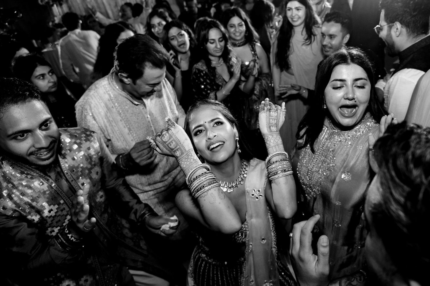A candid black and white shot of celebratory dancing at an Indian wedding reception.