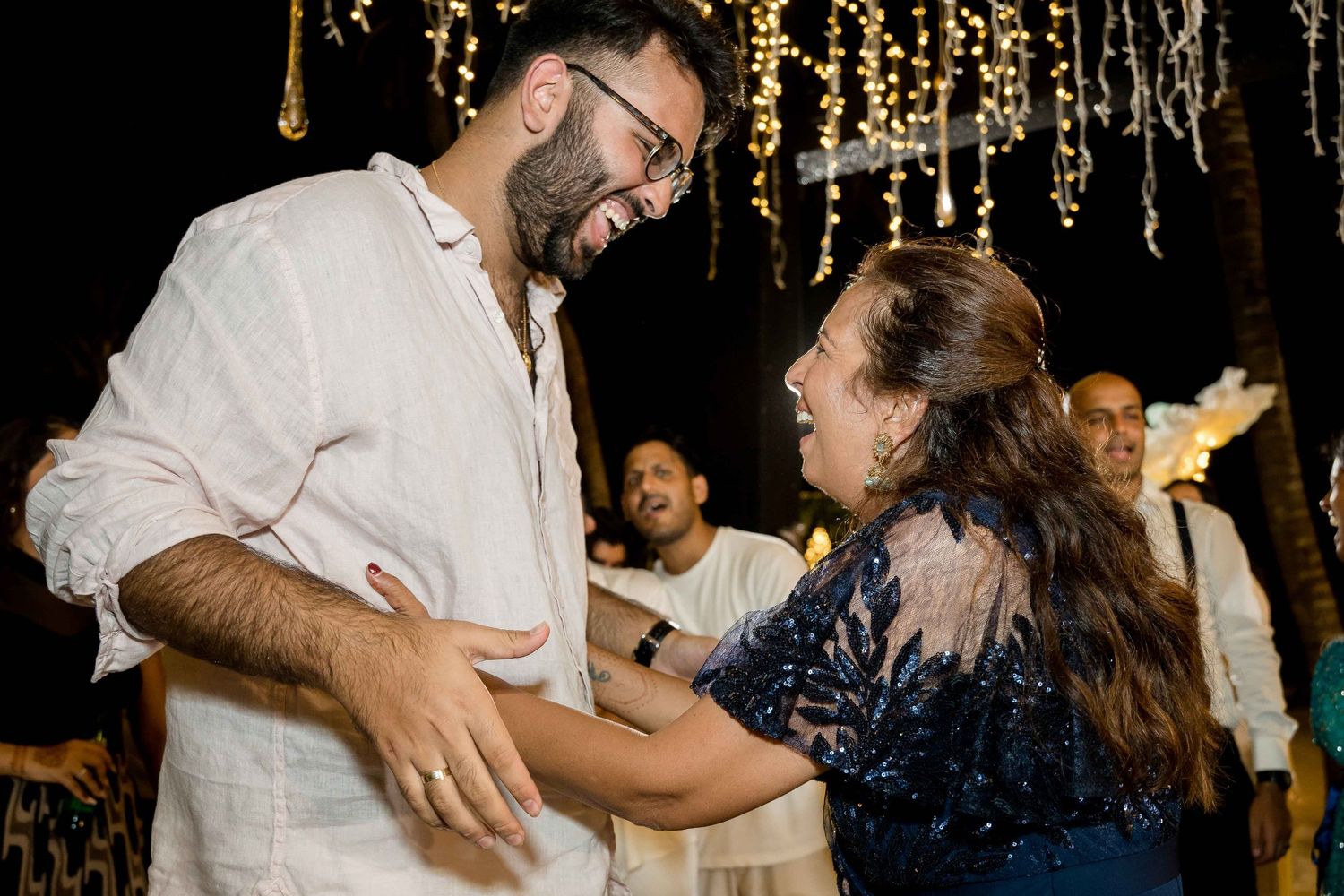 Couples dancing together at a festive wedding reception with glowing string lights overhead.