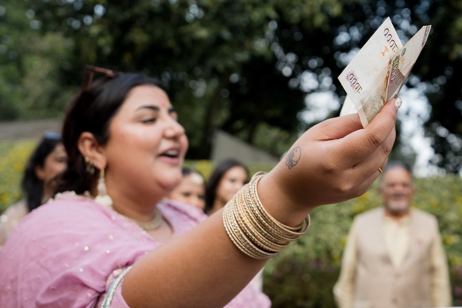 Guest in pink traditional dress holding money during wedding celebrations.