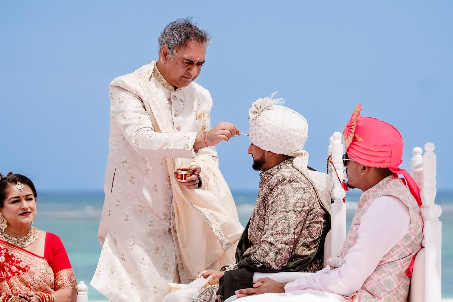 A group of people celebrating a beach wedding ceremony on a sunny day by the ocean.