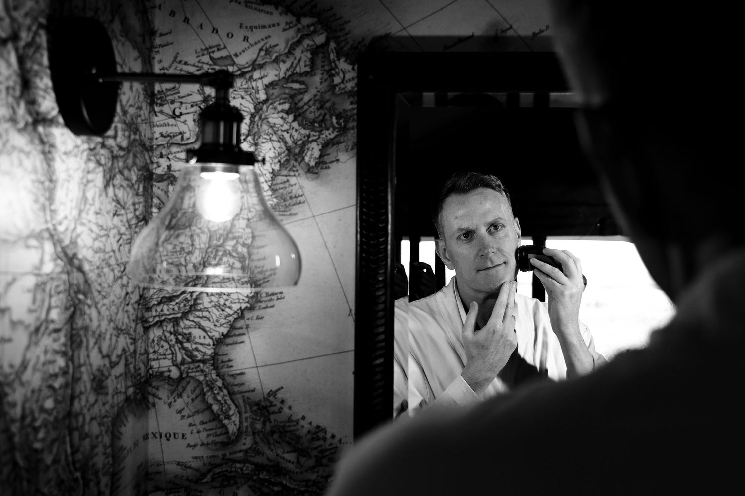 Black and white image of person getting ready in front of mirror with vintage map background.