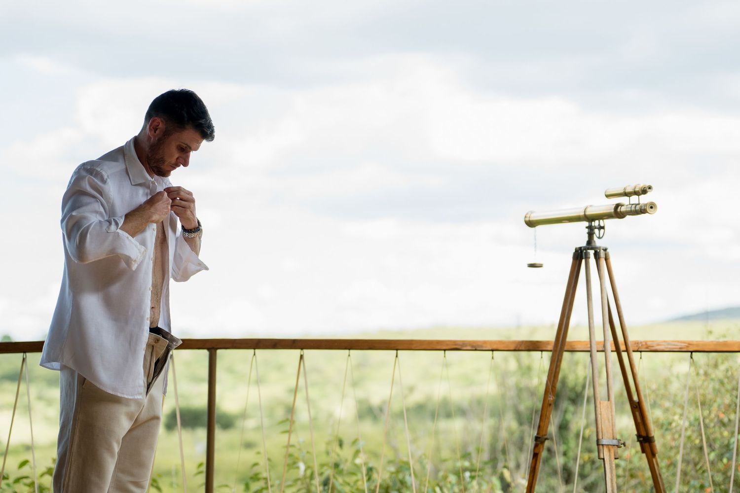 A telescope stands ready on a deck overlooking scenic grasslands.