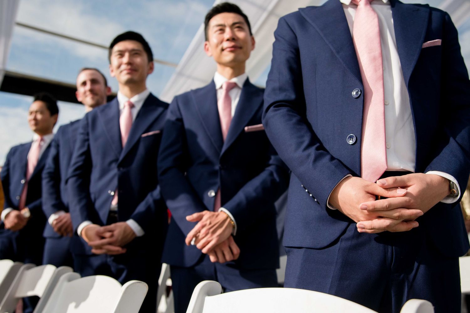Groomsmen in navy suits stand in formation during a wedding ceremony.