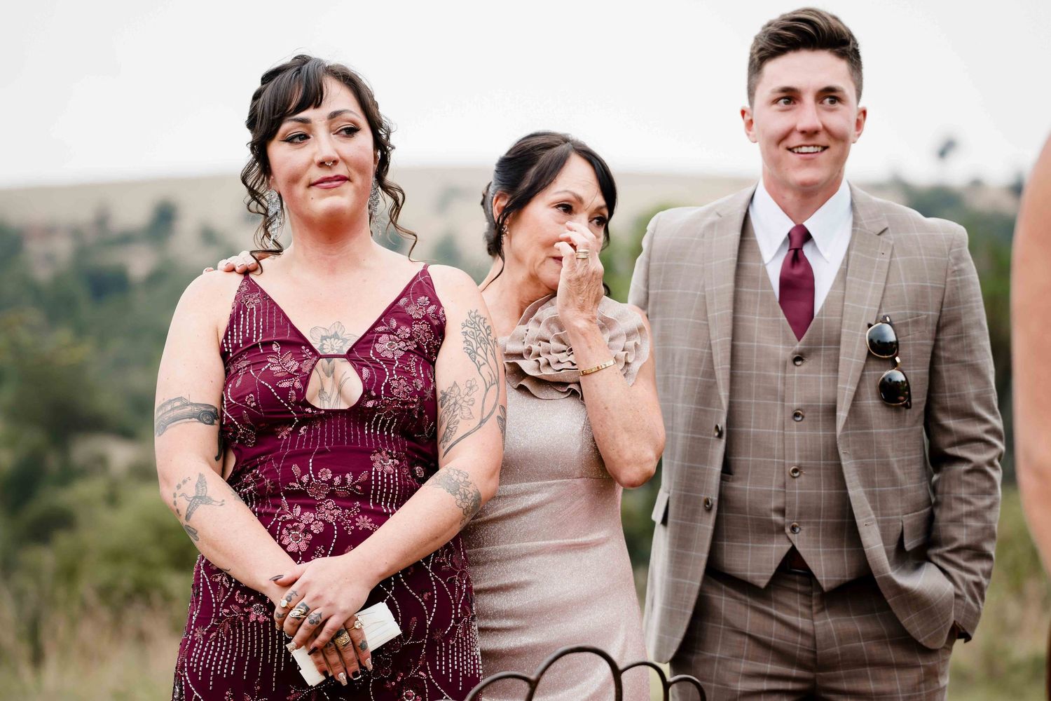 Wedding party in burgundy dresses and tan suits laugh together outdoors during golden hour.