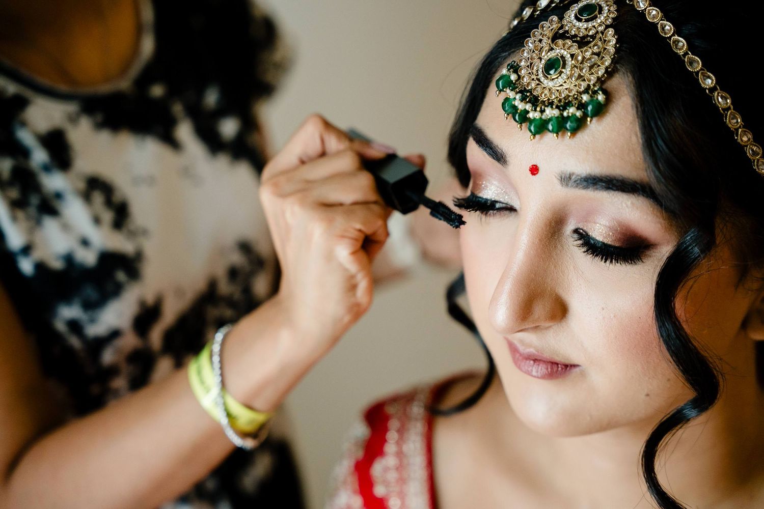 Closeup details of traditional Indian bridal jewelry and makeup with intricate gold and green designs.