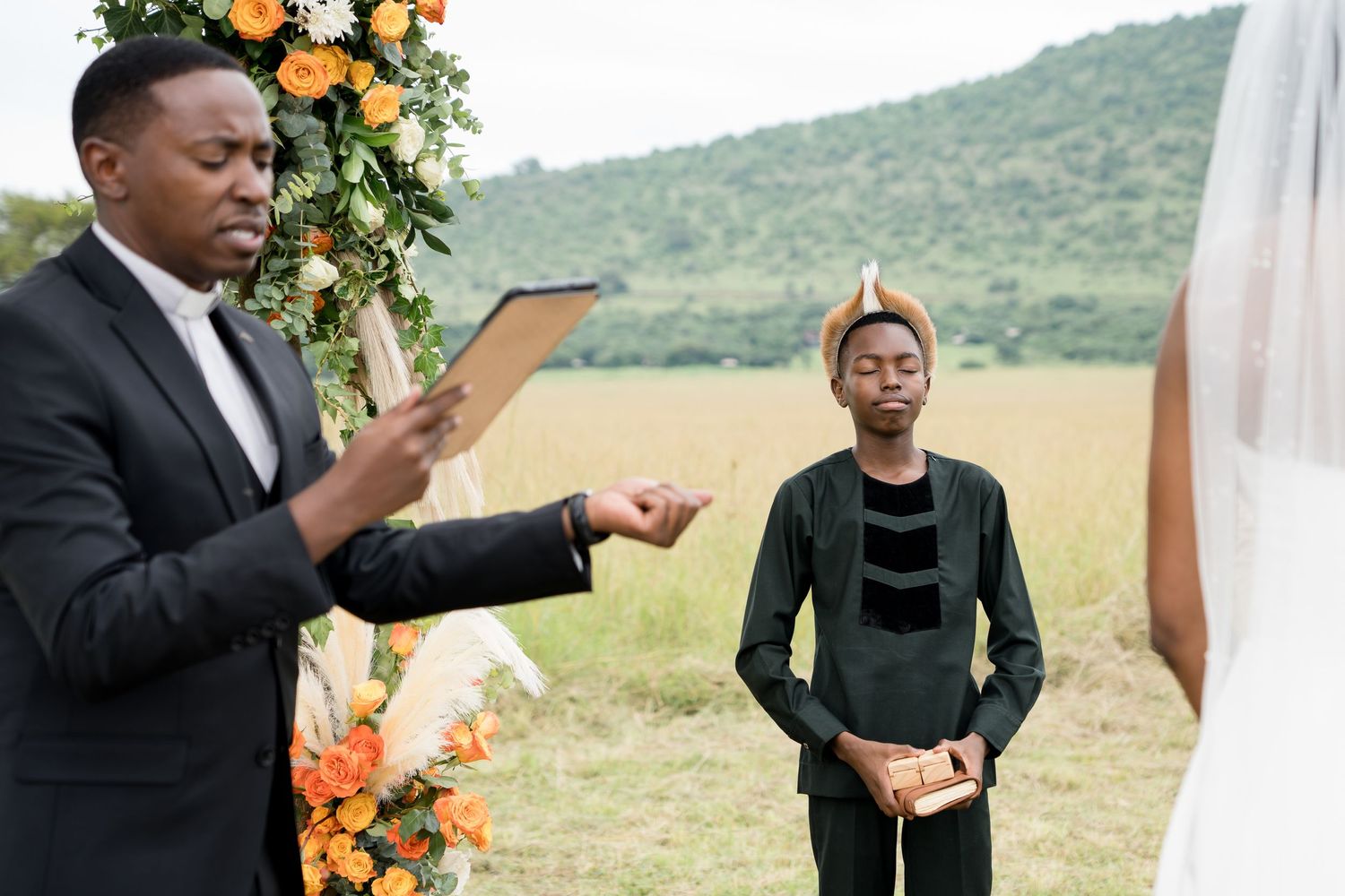 Wedding officiants consulting documents during outdoor ceremony under floral arch.