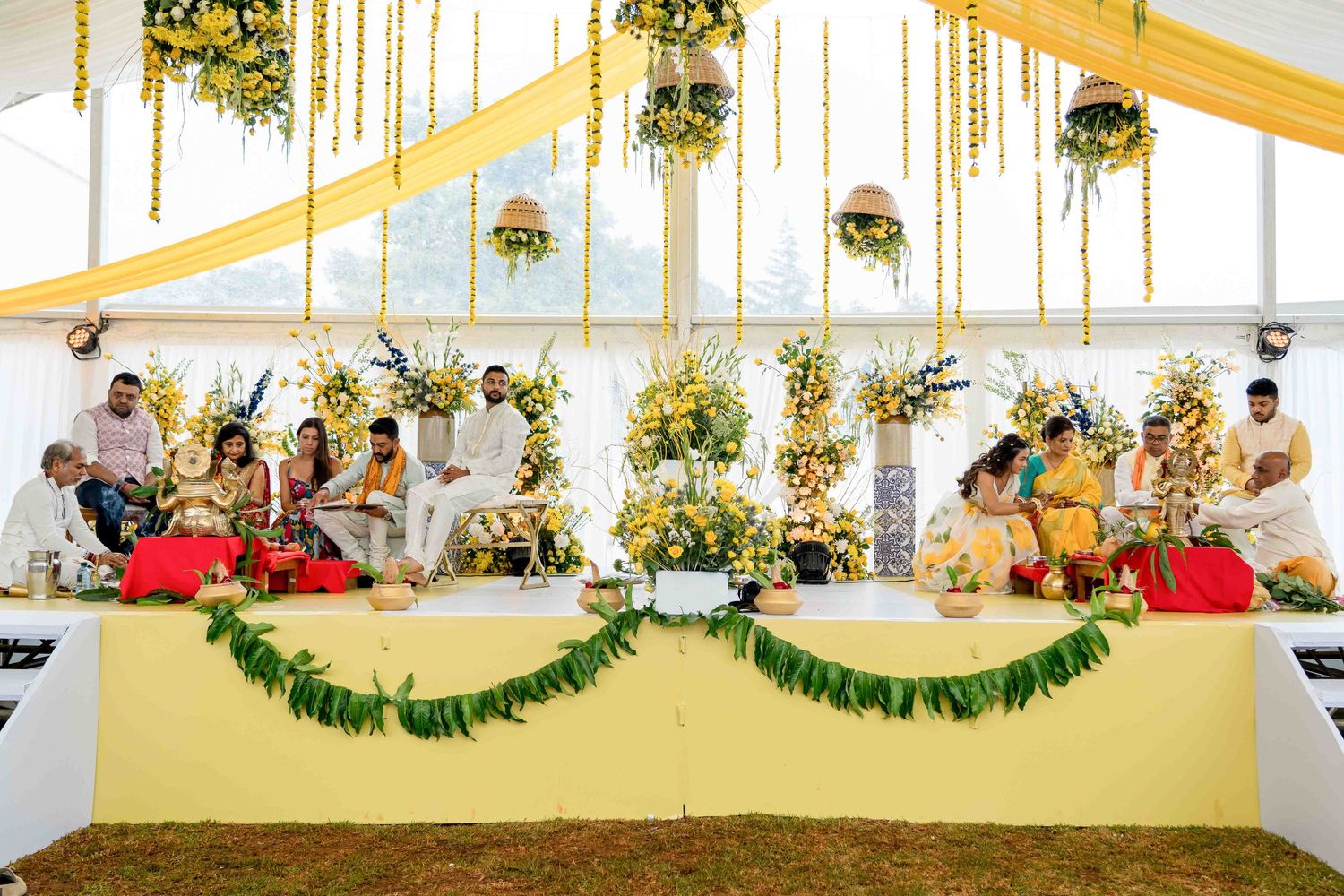 Wedding ceremony setup with yellow and white decor featuring elevated stage and floral arrangements.