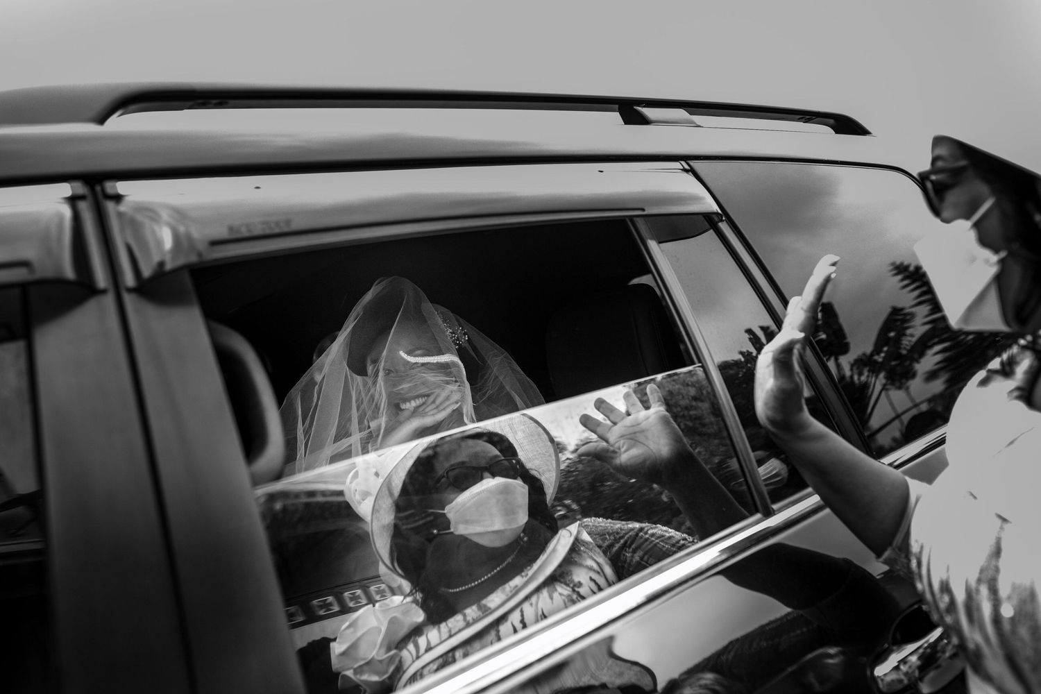 Black and white wedding photo showing a couple getting into a vintage car after their ceremony.