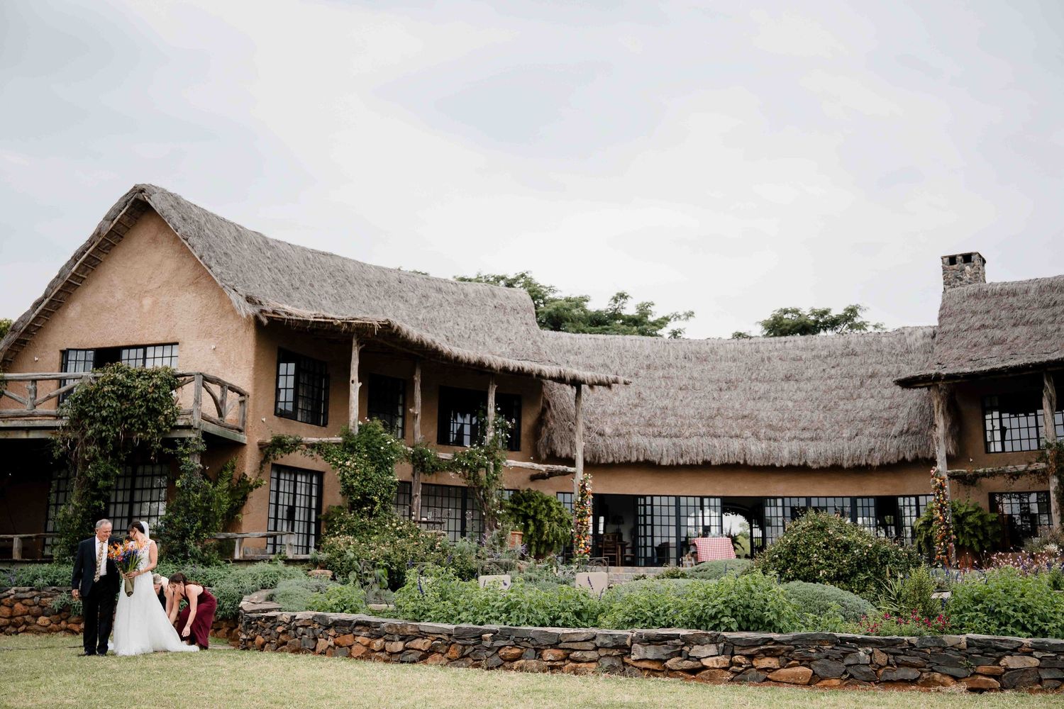 Rustic wedding venue exterior with stone walls and thatched roof shown from multiple angles during an outdoor ceremony.
