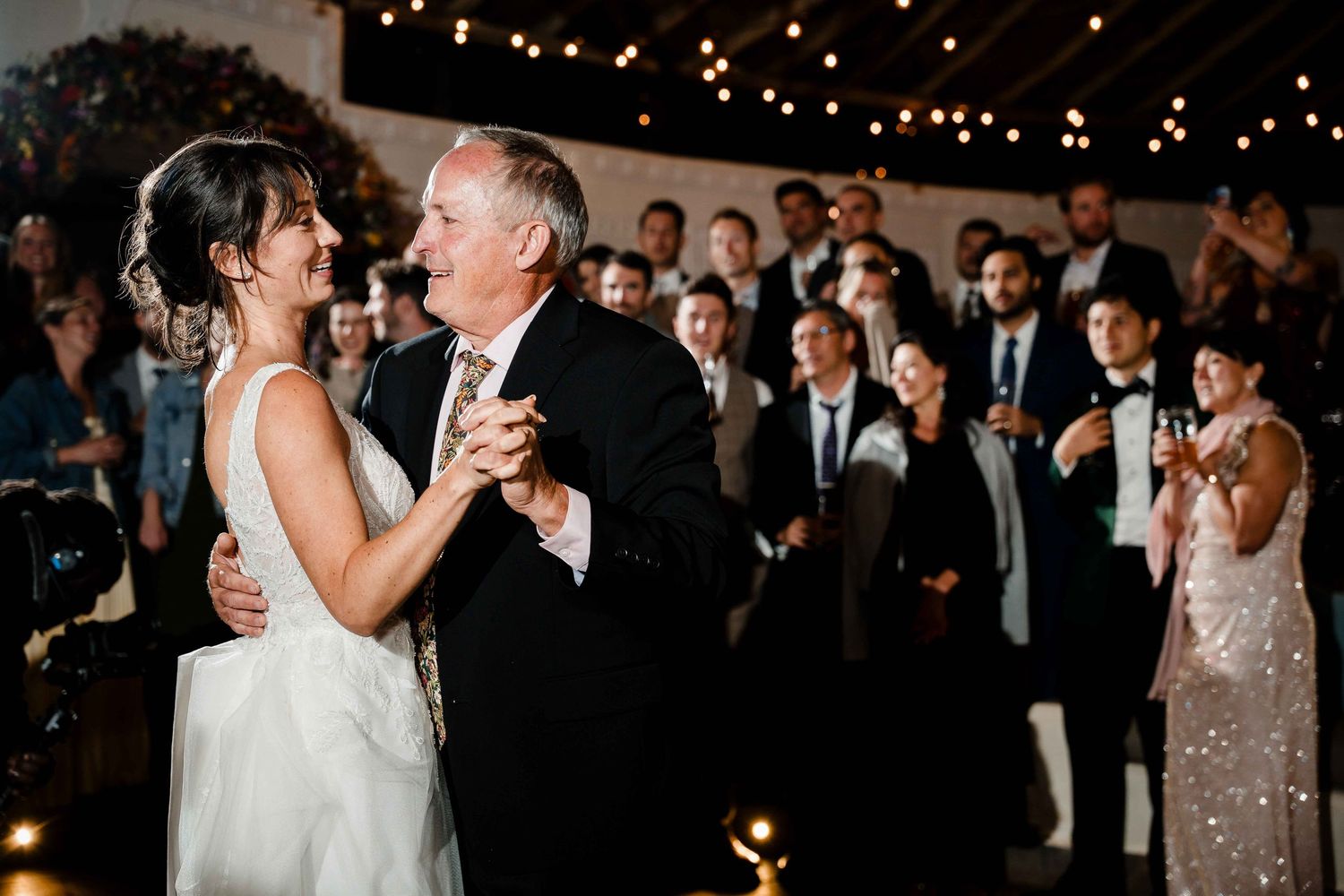 Wedding reception guests dance and celebrate while twinkle lights glow overhead in an elegant venue.