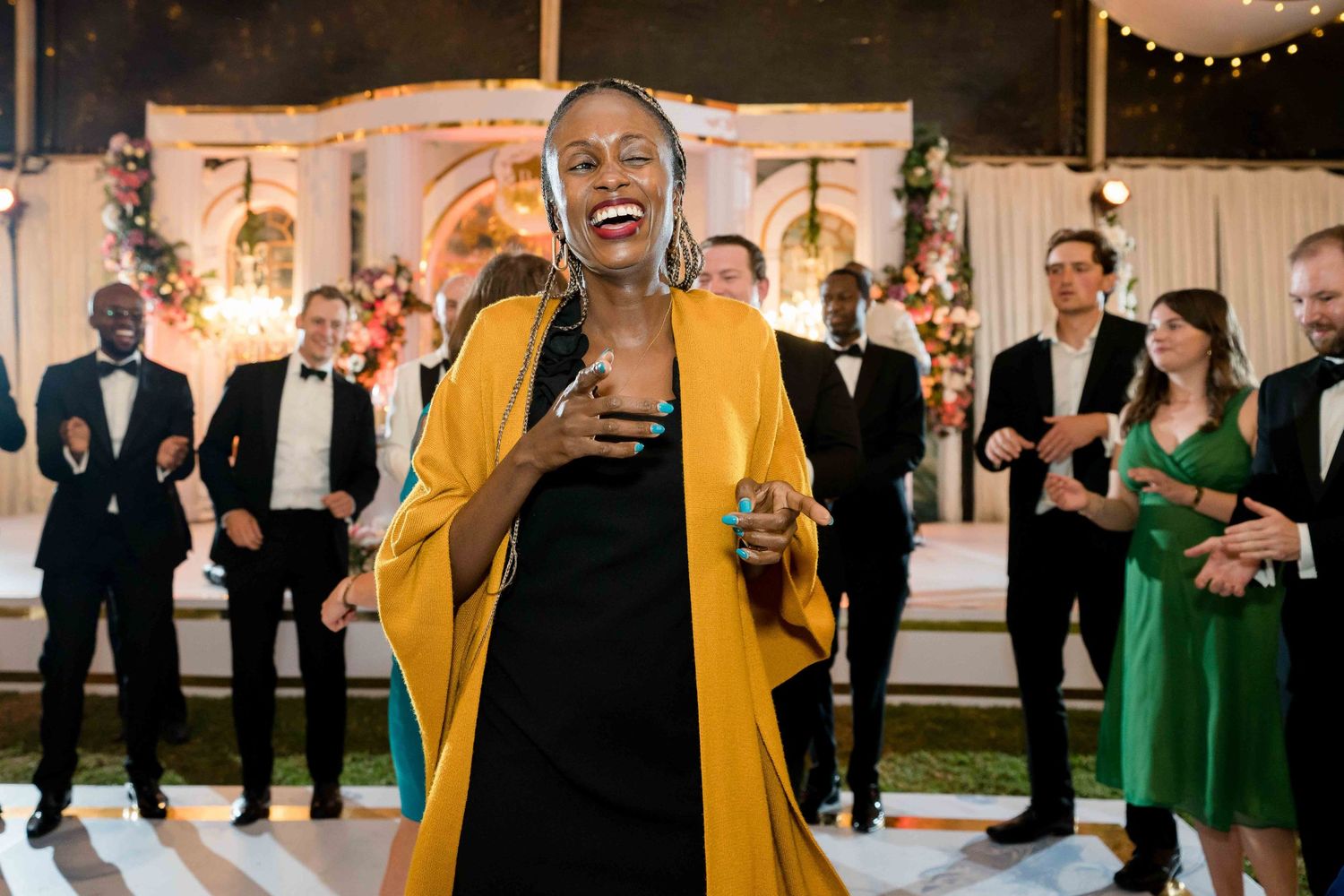 Wedding guests in yellow and green attire dance and celebrate together at an indoor reception venue.