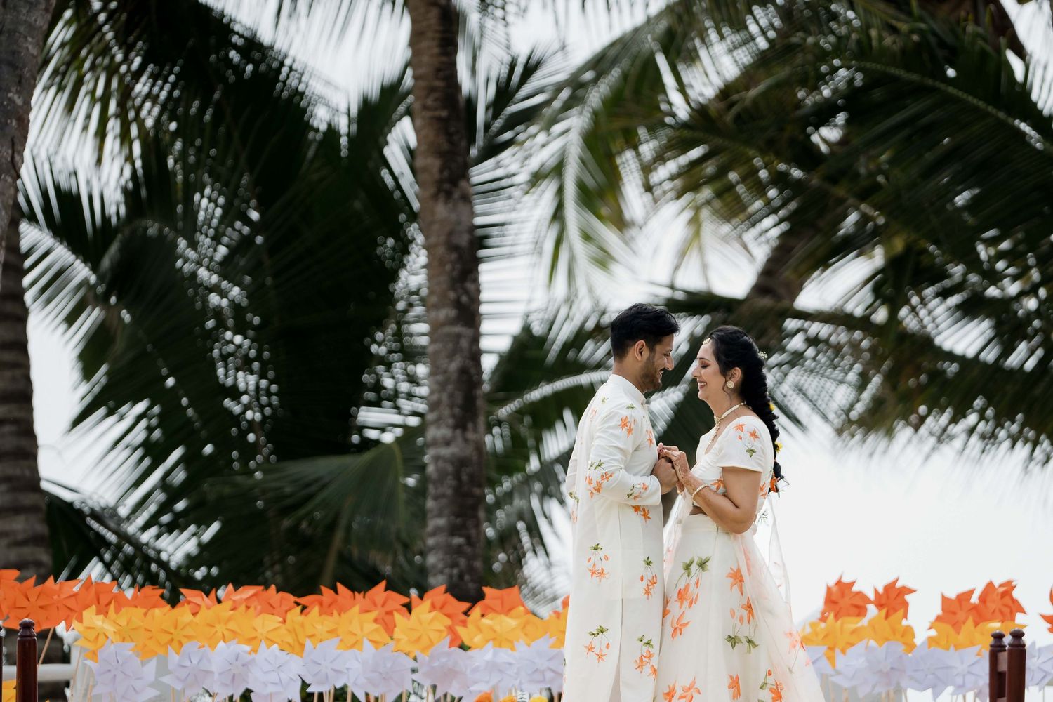 A couple shares a romantic moment under swaying palm trees at a tropical beach wedding ceremony.