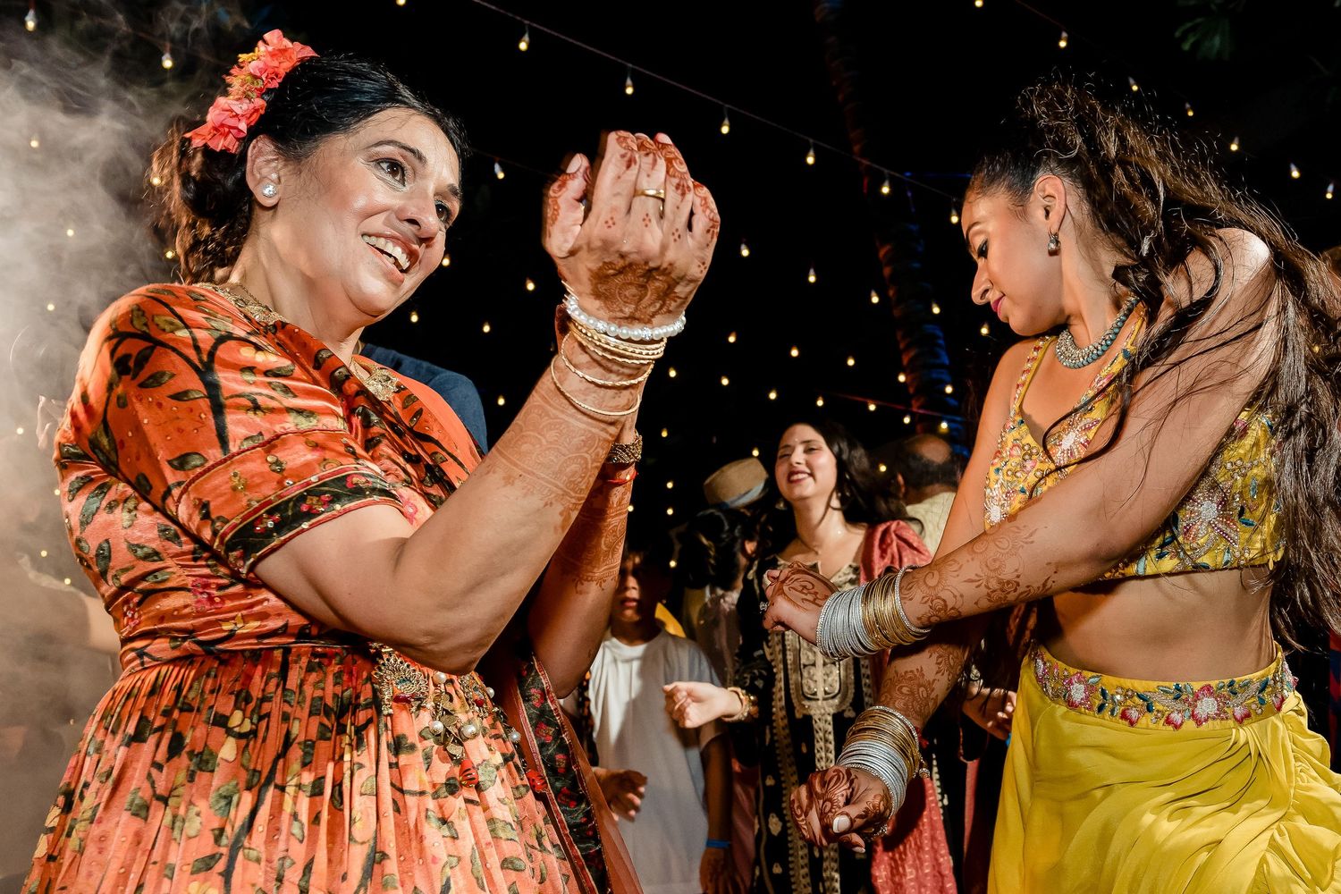 Guests dancing and celebrating at an Indian wedding reception with traditional attire and decorative lighting.