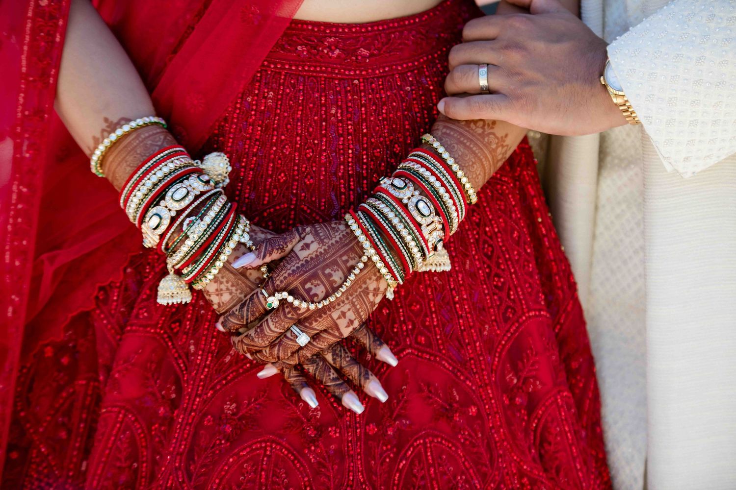Close-up of intricate bridal jewelry and henna on hands with red traditional wedding attire.