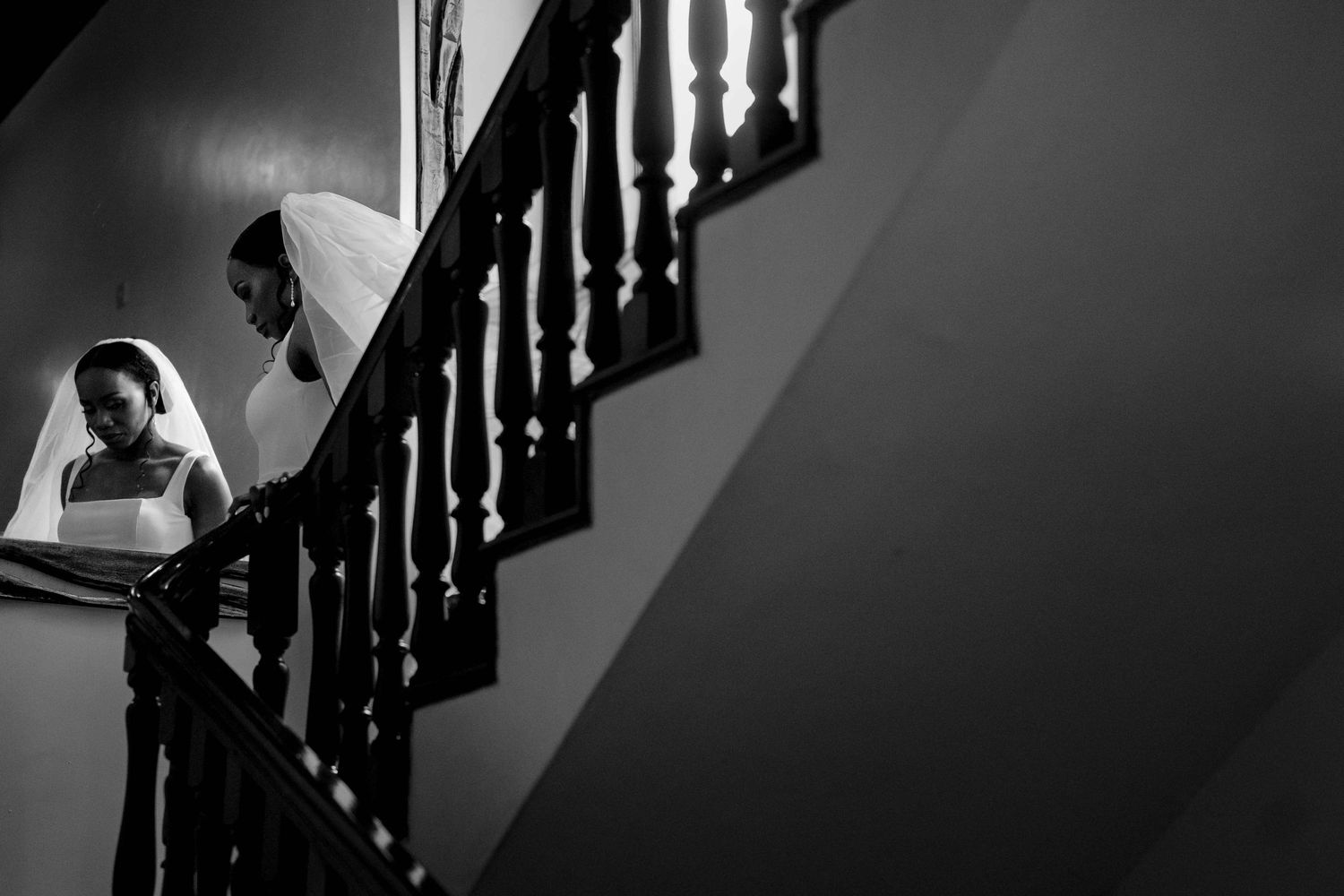 A dramatic black and white photo series of a person ascending a staircase with dark wooden railings and shadows.