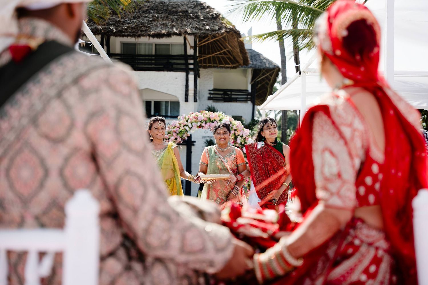 A traditional wedding ceremony with guests in colorful attire gathered outdoors under a covered venue.