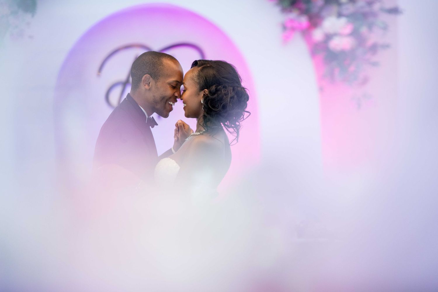 Romantic moment captured through dreamy pink lighting and floral decorations at wedding venue.