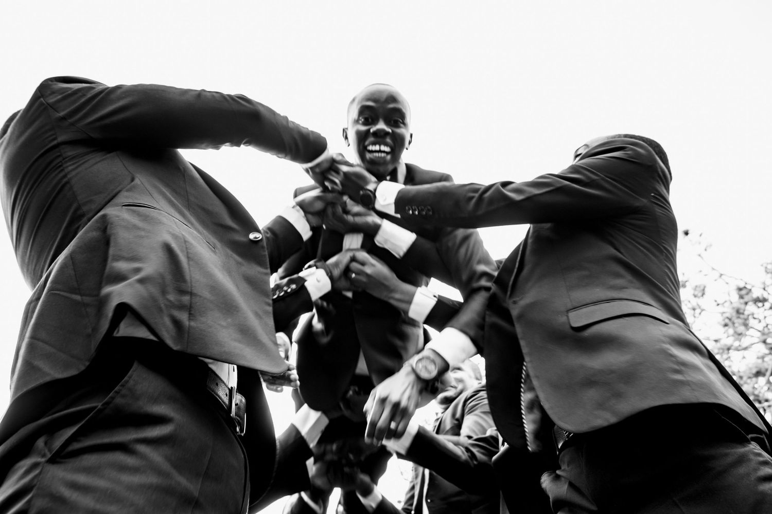 Dynamic low-angle shot captures groomsmen celebrating in black and white.