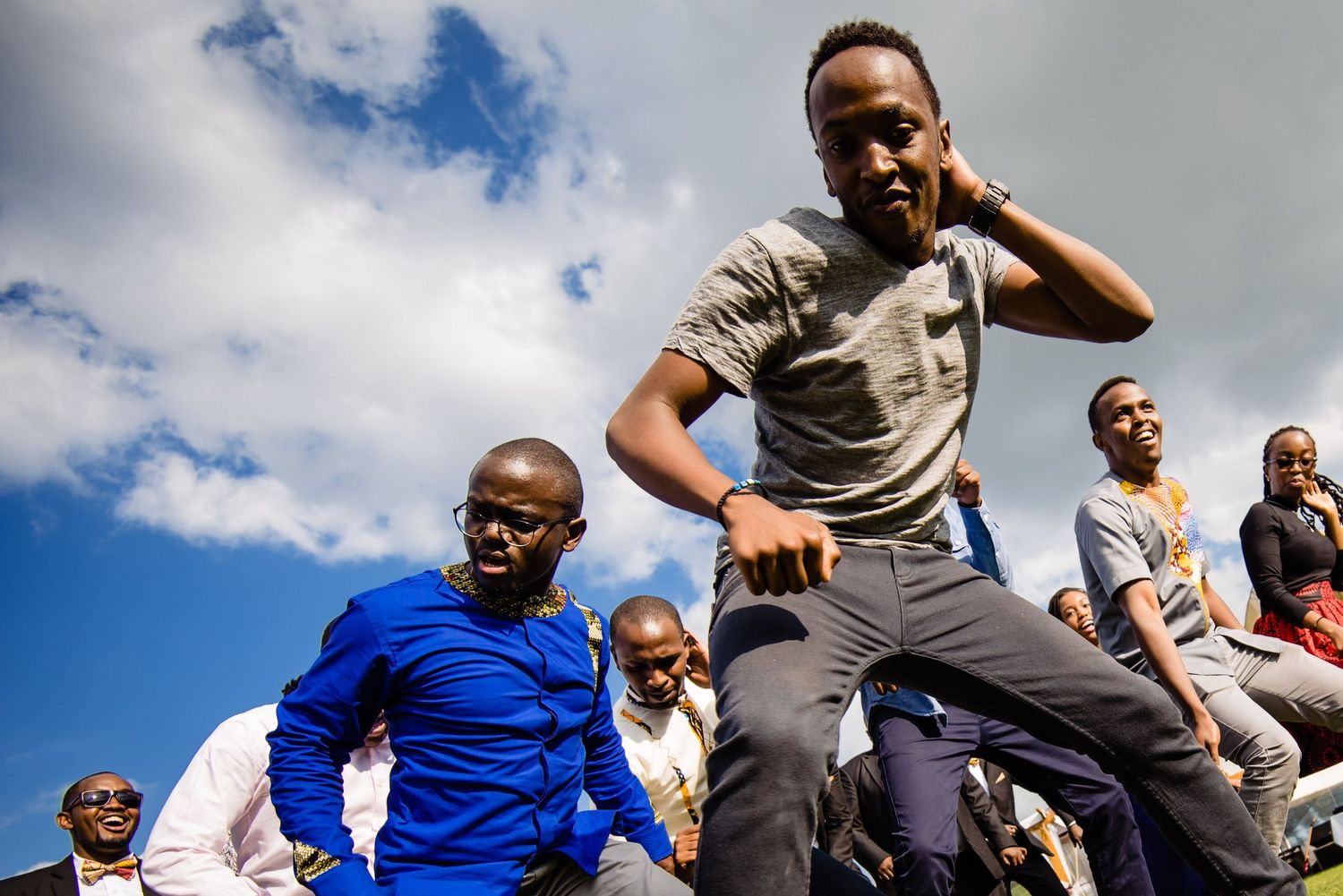 Group of people jumping joyfully against a bright blue sky with white clouds.