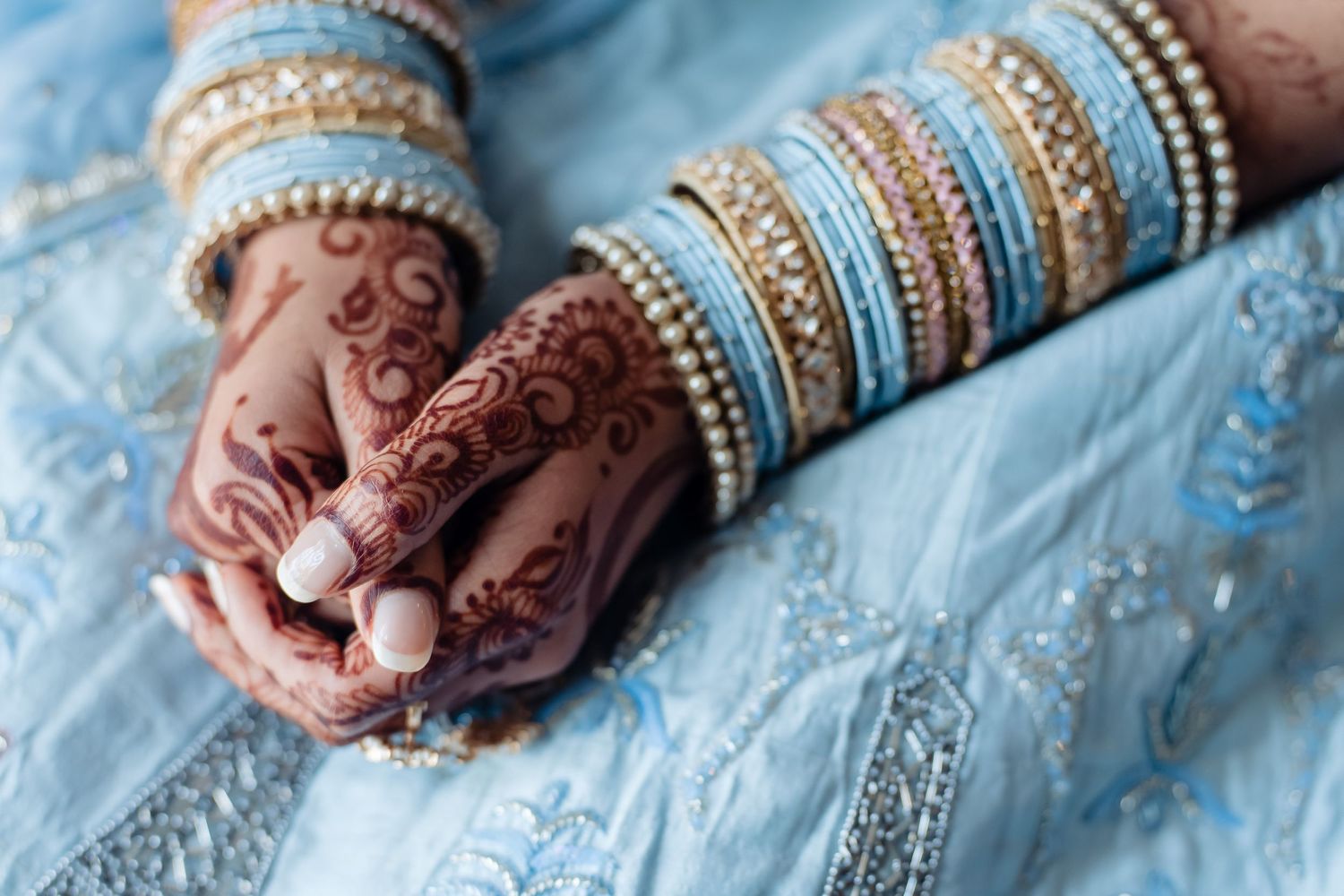 Traditional Indian bridal hands with henna and blue bangles against light fabric.