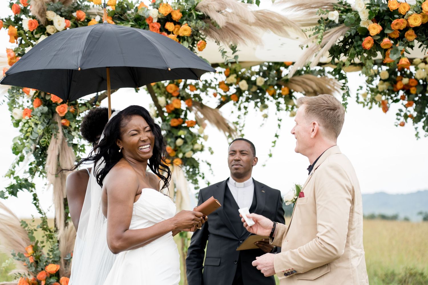 Wedding ceremony under floral arch with umbrella protection on a cloudy day.